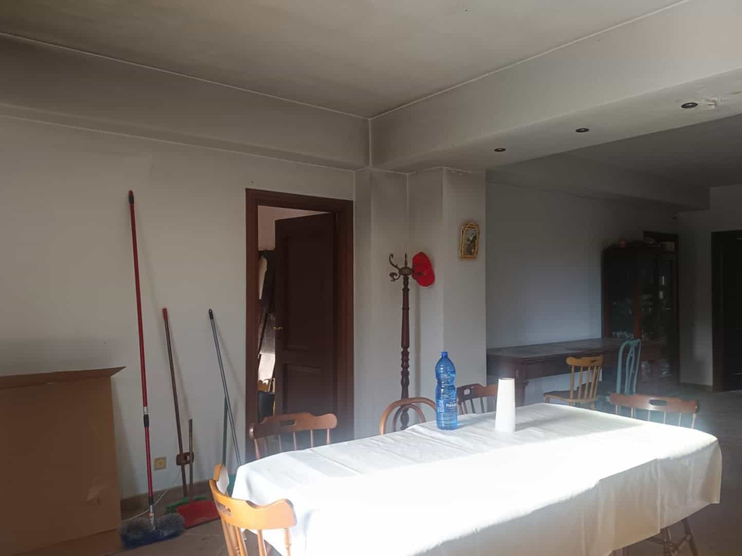 Porte di ingresso in legno in un ambiente domestico con strumenti per la pulizia e mobili in stile classico, illuminato da luce naturale, ideale per una casa accogliente e funzionale.