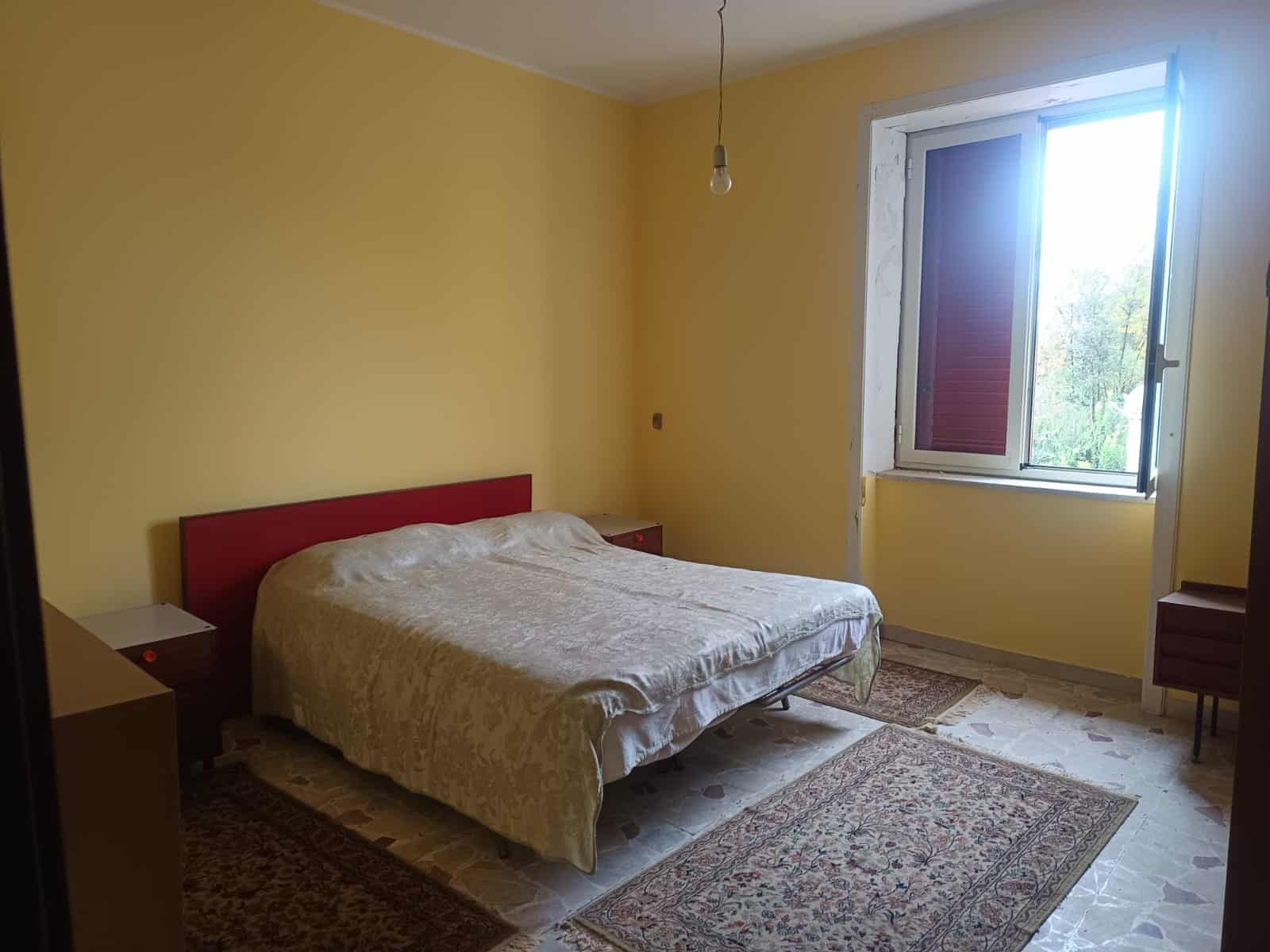 Una stanza da letto luminosa con pareti gialle, un letto matrimoniale con copriletto beige, una finestra aperta che lascia entrare luce naturale, e tappeti tradizionali sul pavimento in parquet, ideal.