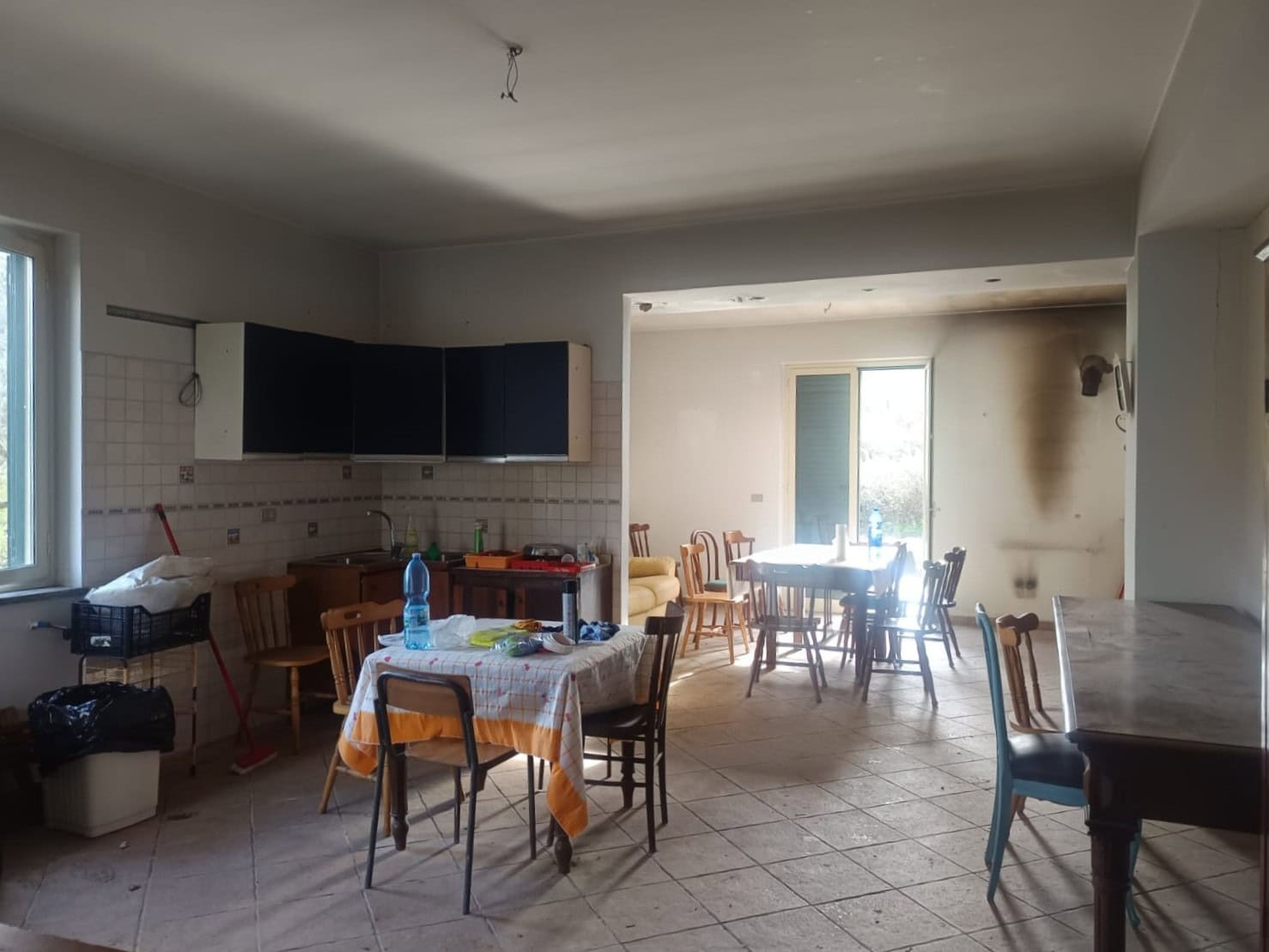 Ampia cucina abitabile con tavolo centrale, sedie in legno, cucina moderna con armadietti scuri, finestra luminosa, ambiente spazioso e luminoso, ideale per famiglie e incontri conviviali.