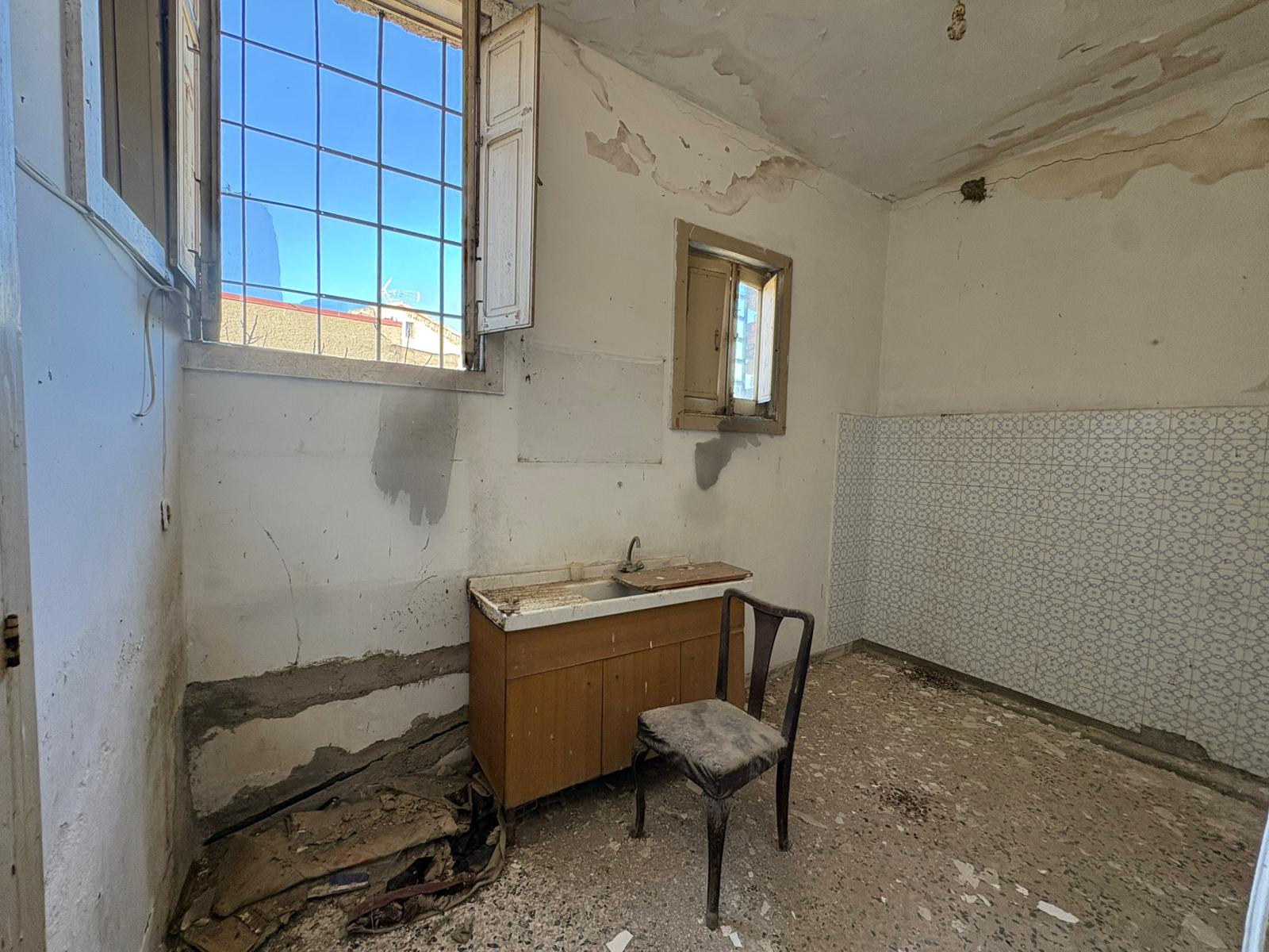 Vaschetta da cucina vecchia e rovinata in una stanza abbandonata con pareti danneggiate e pavimento sconnesso, ambiente trascurato e in stato di degrado.