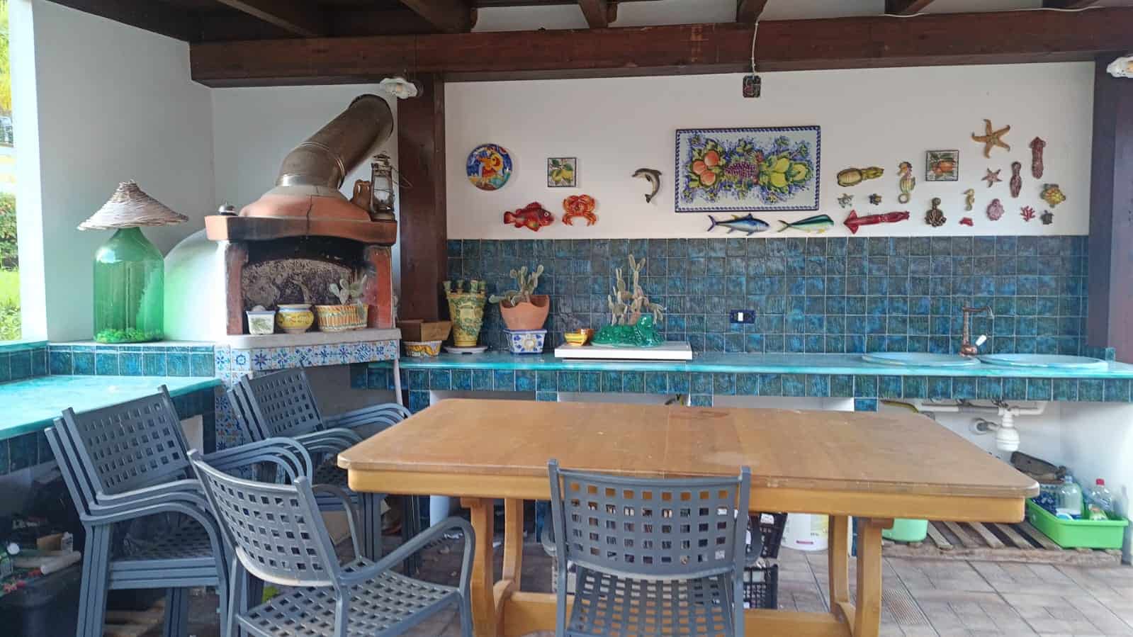 Tavolo da pranzo in legno con sedie in plastica in un'area esterna coperta, decorata con oggetti marini e piante, ideale per convivialità e relax all'aperto.
