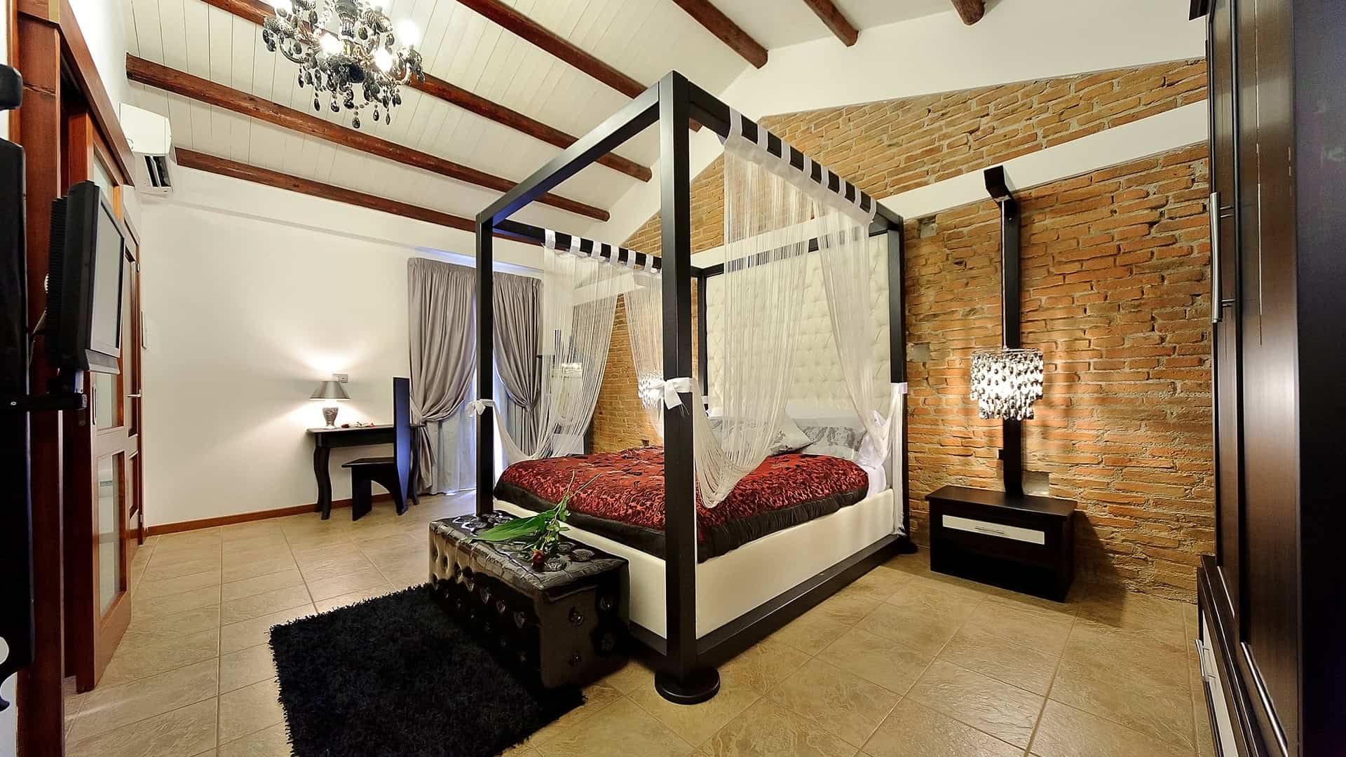 Elegante camera da letto con letto a baldacchino, pareti in mattoni a vista e arredi moderni, ideale per affitti di case vacanza o residenziali di alta qualità.