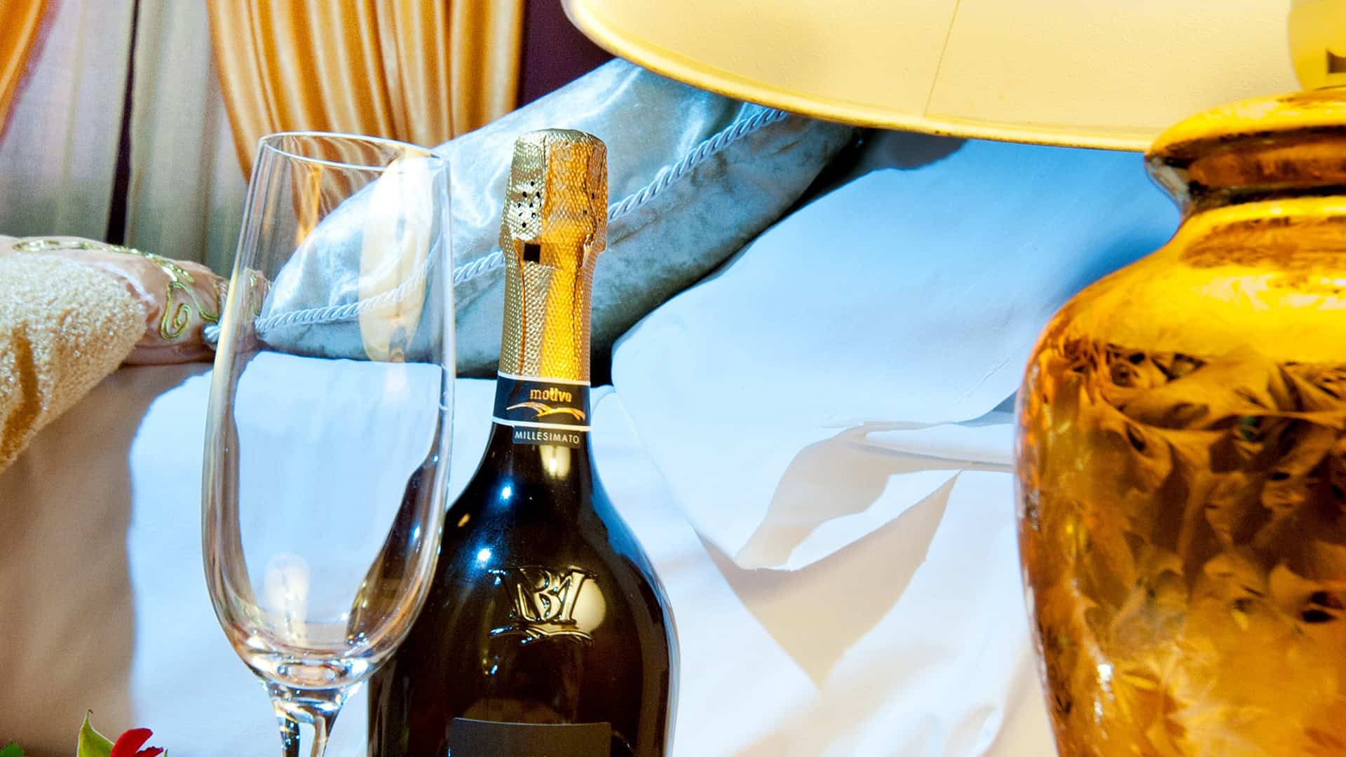 Bottiglia di champagne e bicchiere vuoto su comodino in camera da letto elegante, atmosfera di lusso e comfort.