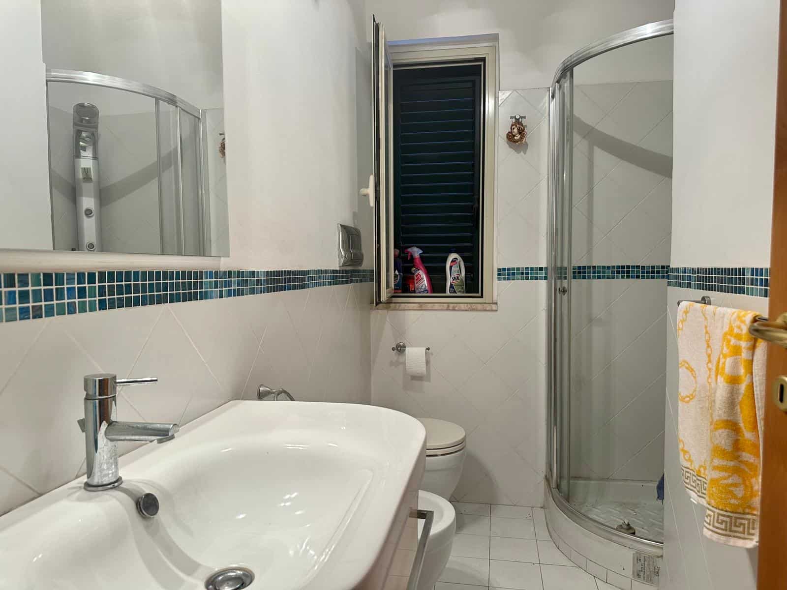 Lavabo moderno con box doccia in bagno spazioso, illuminato da finestra, arredato con accessori eleganti e funzionali, ideale per ambienti di comfort e stile.