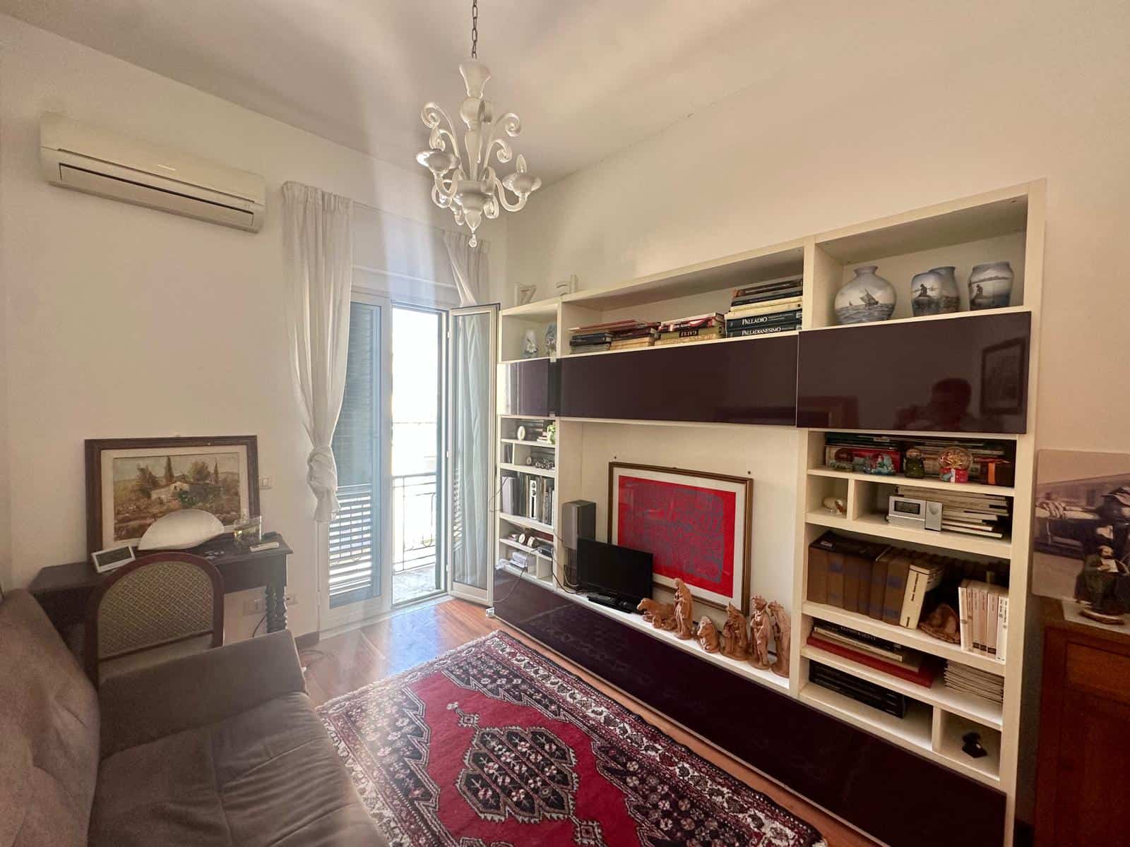 Interno soggiorno moderno con libreria, TV e decorazioni, illuminato da luce naturale, arredamento elegante e dettagli di design, ambiente accogliente e ben organizzato.