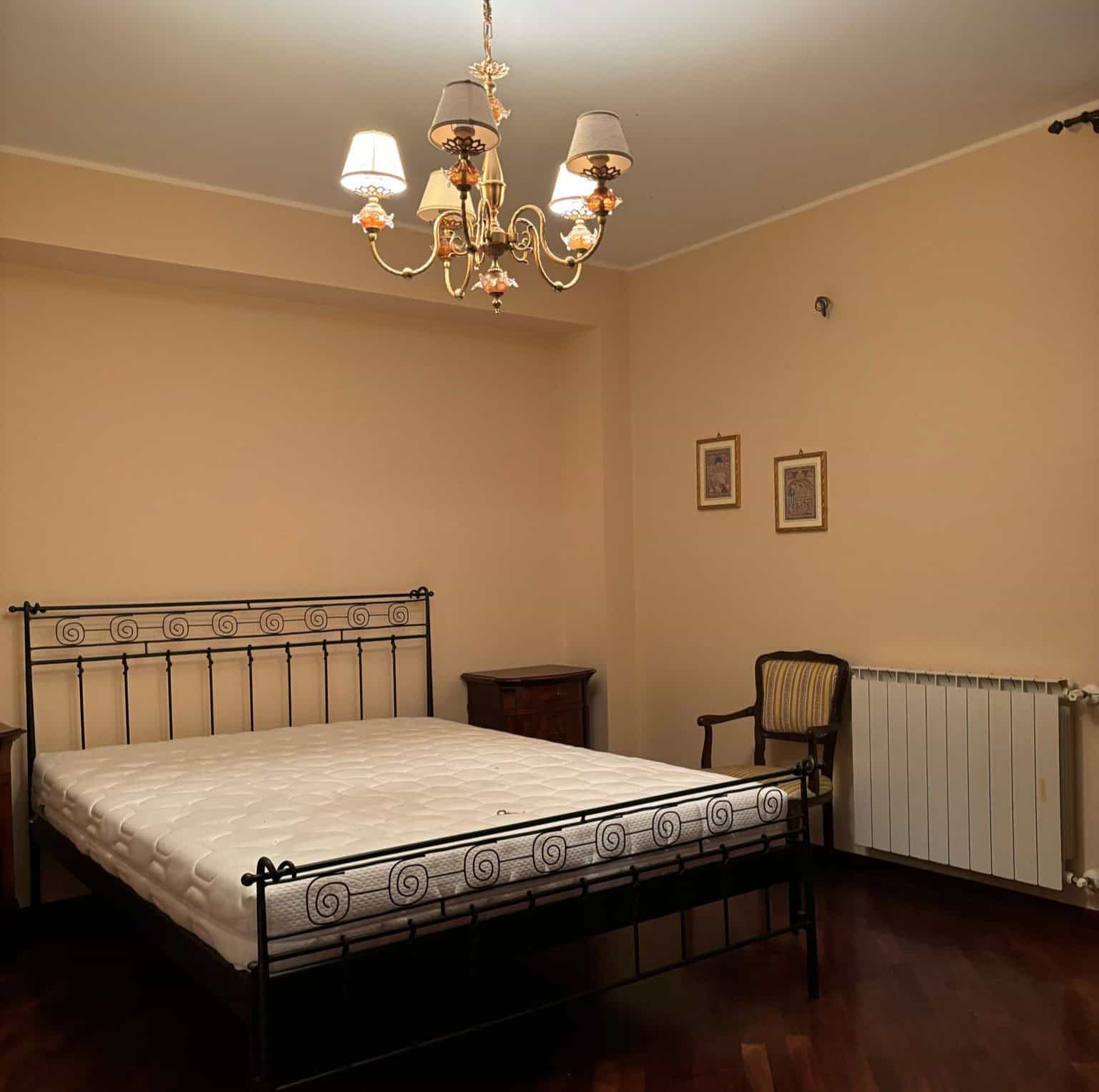 Camera da letto con letto in ferro battuto, lampadario elegante e arredi classici in un ambiente accogliente.