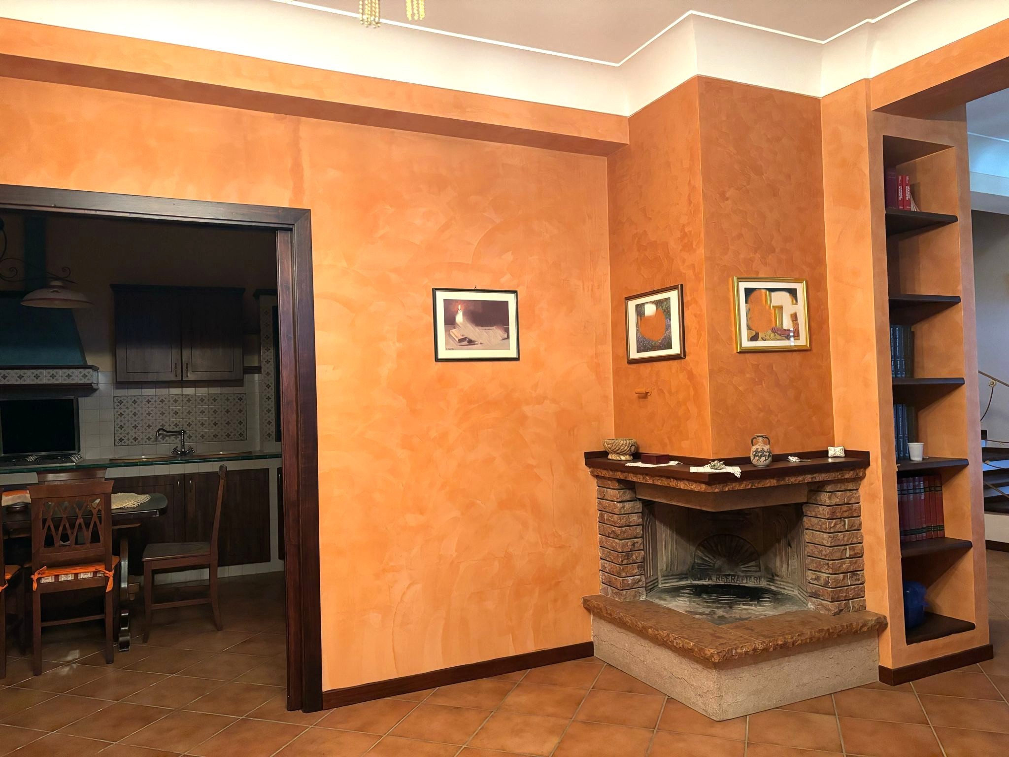 Il camino in mattoni in soggiorno con pareti arancioni e libreria a destra, ambiente accogliente e elegante.