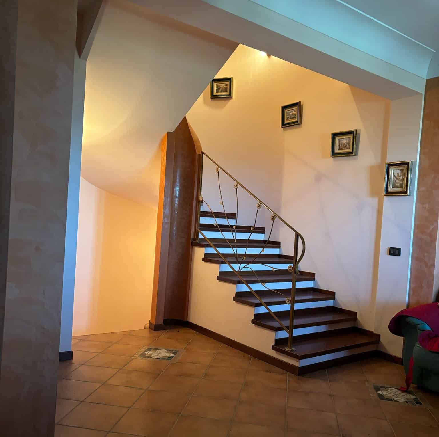 Scale interna con gradini in legno e ringhiera in metallo, situata in un ambiente domestico accogliente e ben illuminato, ideale per l'accesso ai piani superiori di una casa moderna.
