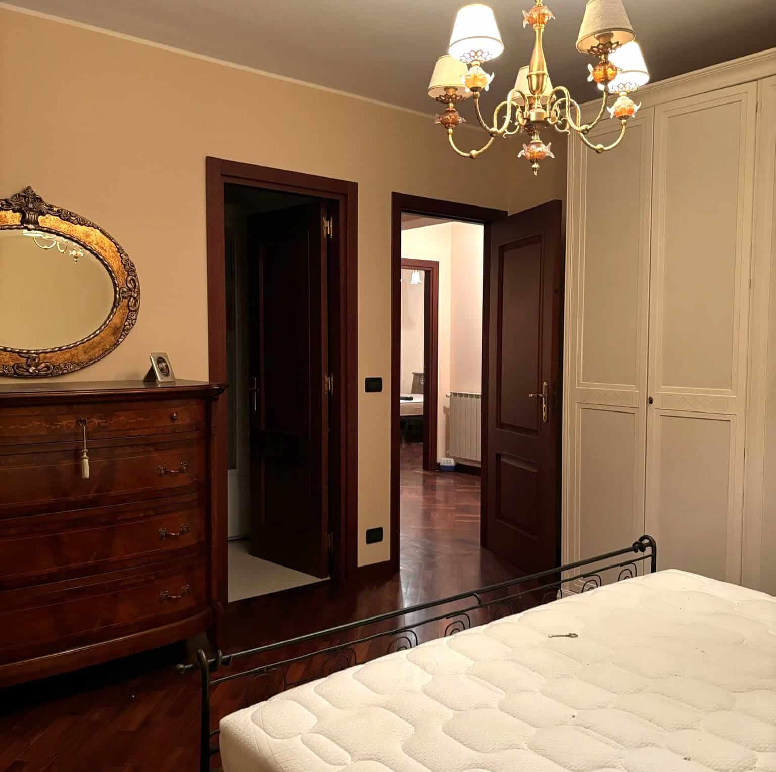 Aria di casa: camera da letto con mobili classici, armadio a muro e lampadario elegante, ambiente accogliente e ben arredato. Perfetta per vivere momenti di relax e comfort domestico.