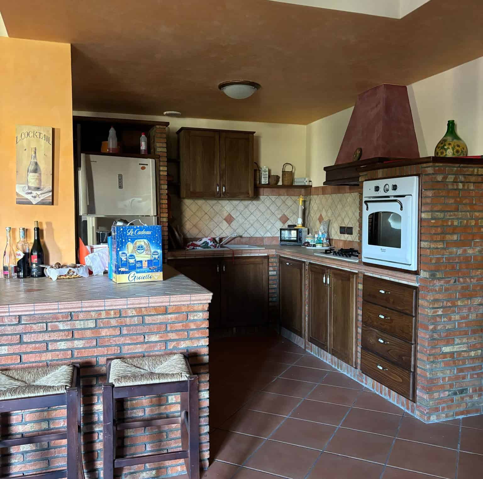 Un ALT tag: Cucina moderna con mobili in legno scuro, parete in mattoni rossi e angolo cottura con forno e piano cottura, ambiente accogliente e ben arredato.