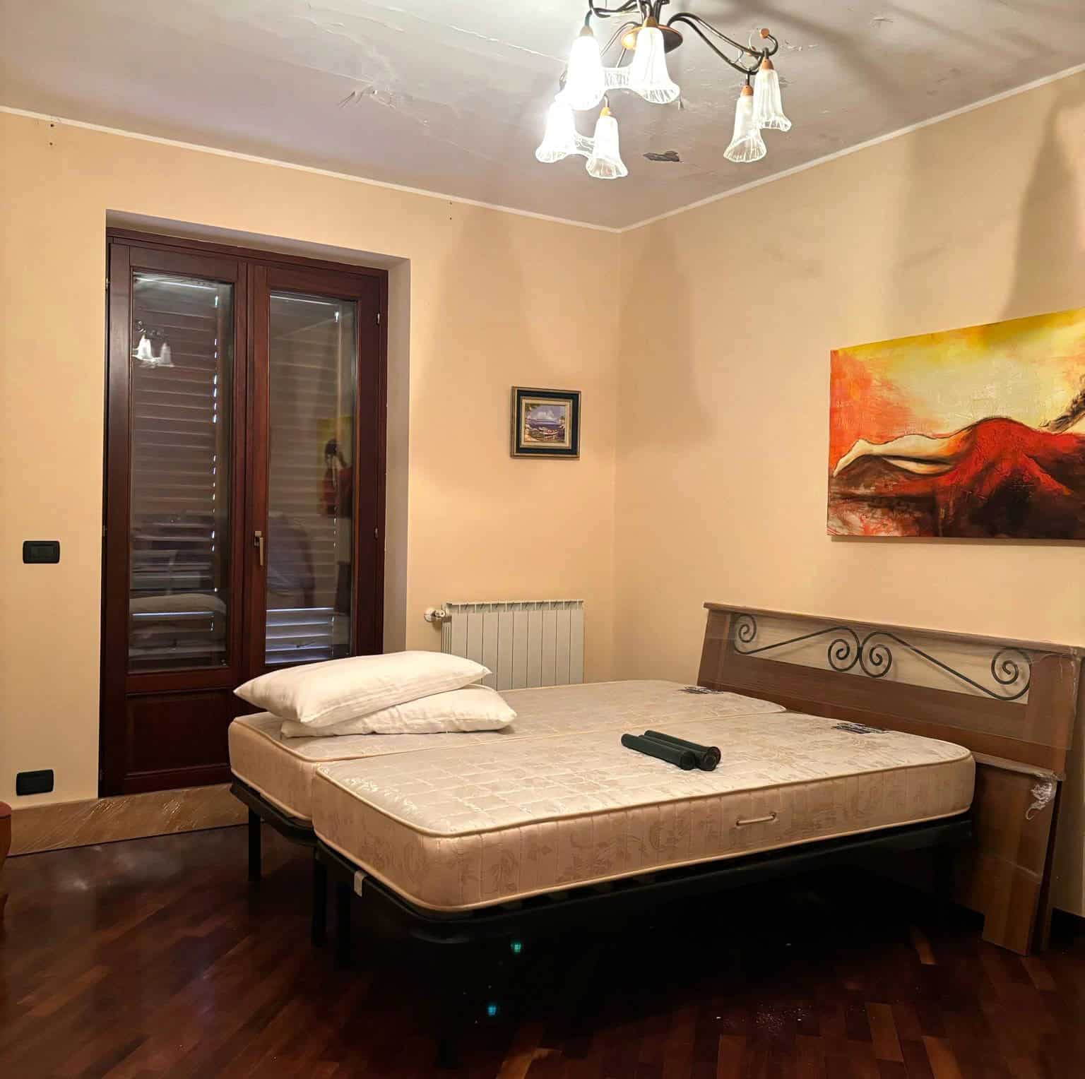 Camera da letto con letto matrimoniale, finestra con persiane e decorazioni artistiche, ambiente accogliente e ben illuminato.