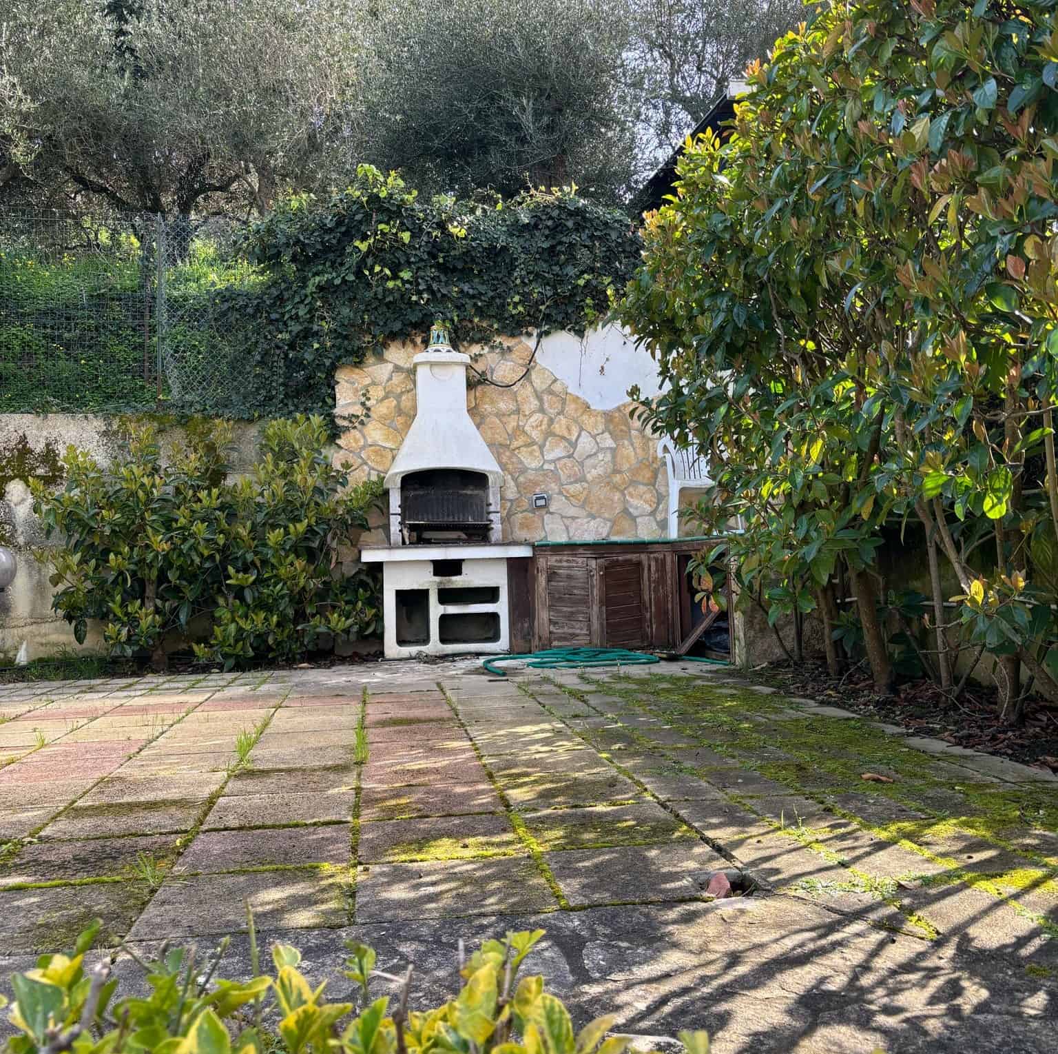Barbecue in giardino con panchina in pietra e piante verdi, spazio esterno ideale per cene all'aperto e relax. Ambiente tranquillo e ben curato, perfetto per vivere momenti conviviali all'aperto.