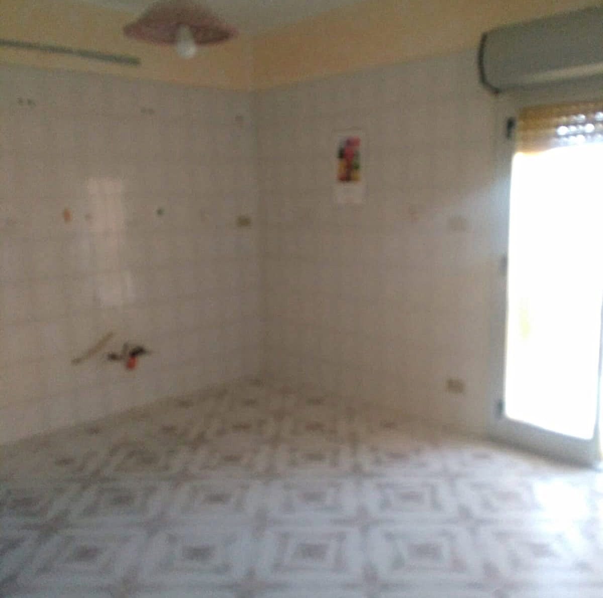 Cucina vuota in fase di ristrutturazione con pareti in piastrelle e grande finestra con accesso al balcone.
