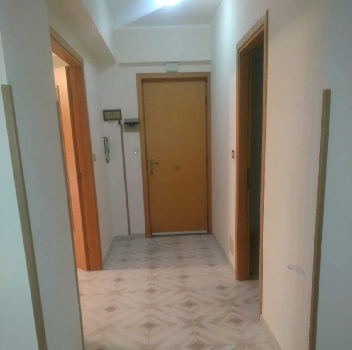 Porta d'ingresso in un appartamento con pareti bianche e pavimento in piastrelle decorative, vista di un corridoio con porte interne e sistema di sicurezza.
