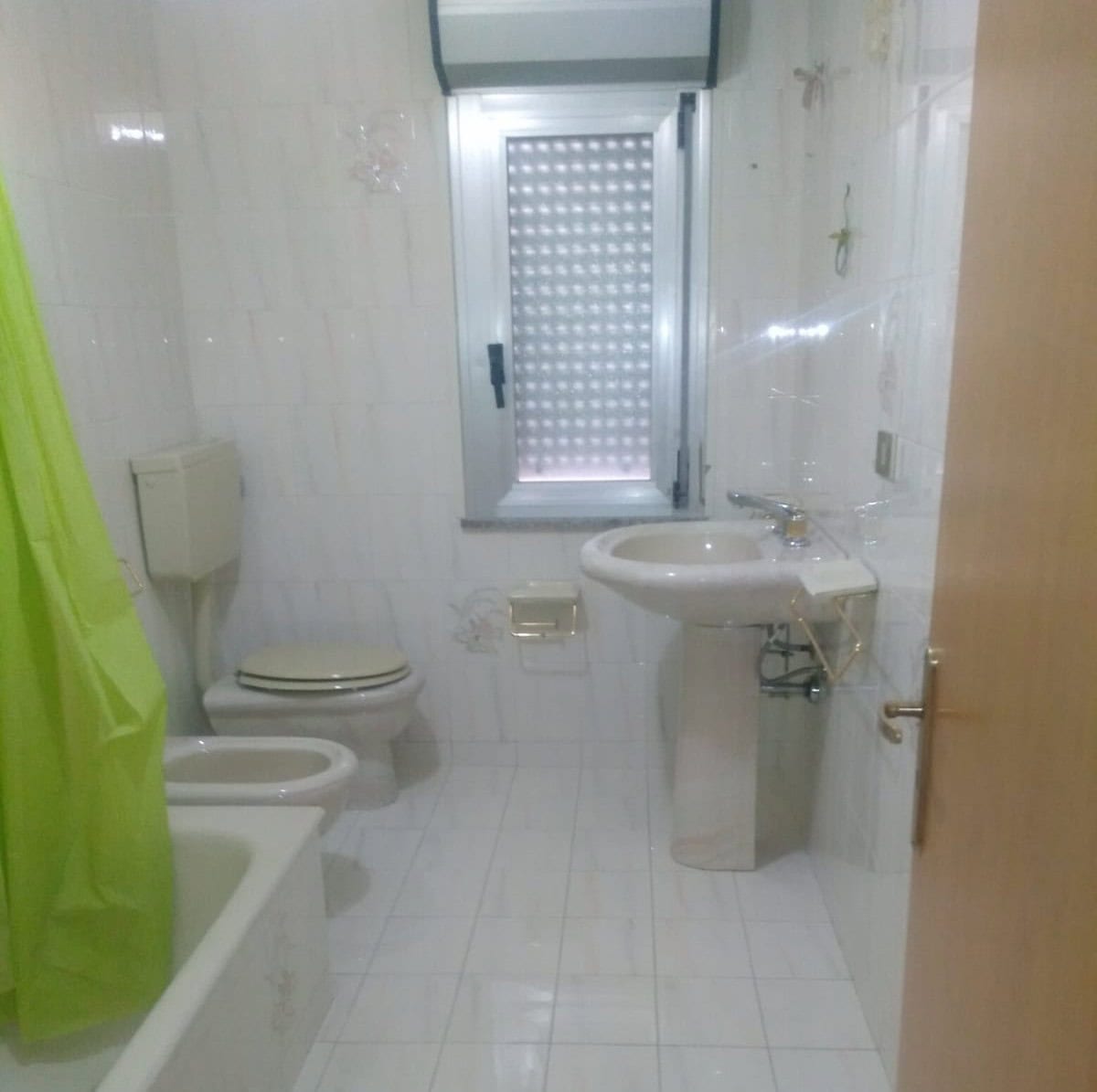 Lavabo e servizi igienici in un bagno semplice e funzionale con finestra, piastrelle bianche e accessori essenziali, ideale per appartamenti e case.