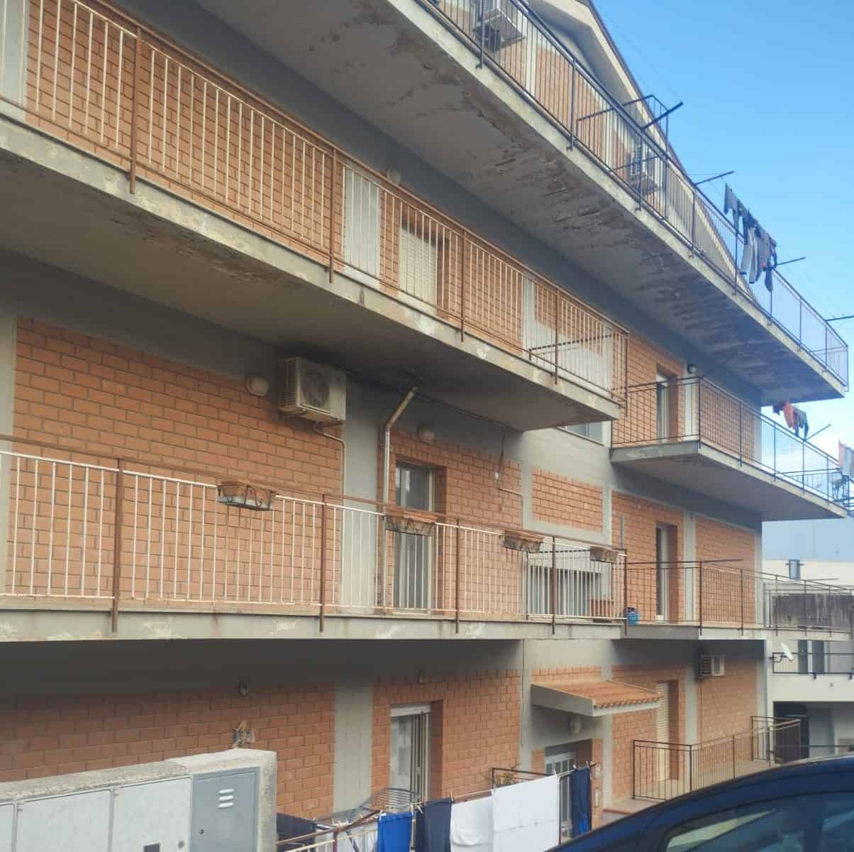 Balcone di un edificio residenziale in mattoni con ringhiere in metallo e stendibiancheria all'aperto, sotto un cielo azzurro.