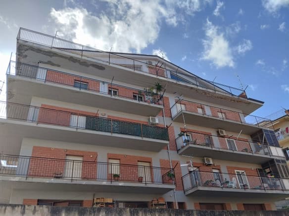 Appartamento residenziale con balconi e aria condizionata, edificio moderno in zona urbana, vista panoramica sul cielo e sulle nuvole, struttura in mattoni e cemento, ideale per vivere in città.