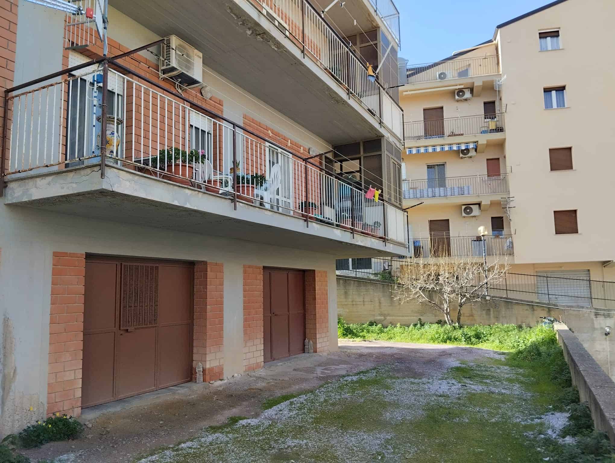 Appartamenti con balconi e garage in edificio residenziale a città, vista esterna, dettagli architettonici e spazi verdi circostanti.