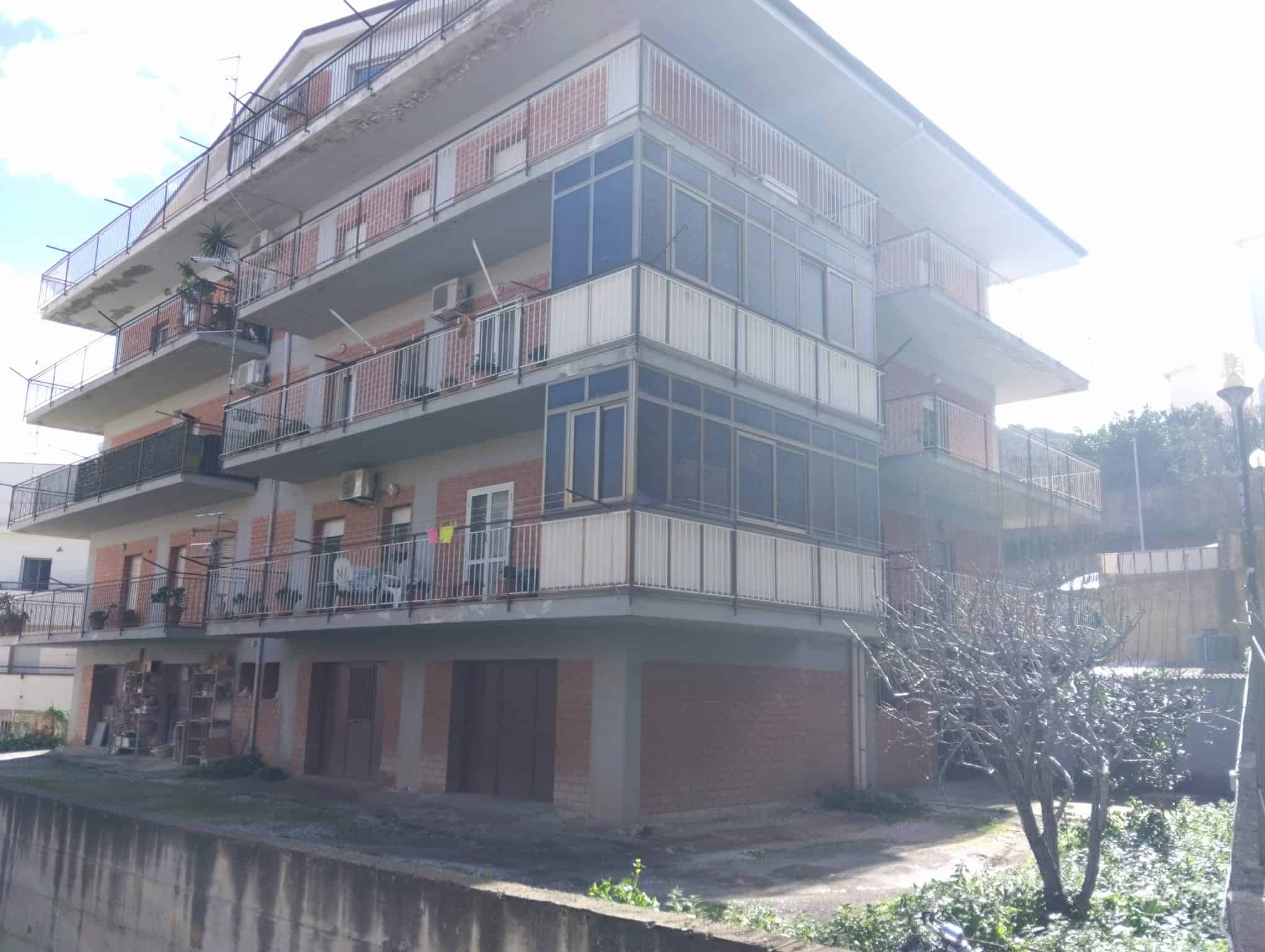 Edificio residenziale con balconi e veranda, struttura moderna in mattoni e vetro, situato in zona tranquilla con giardino e alberi circostanti.