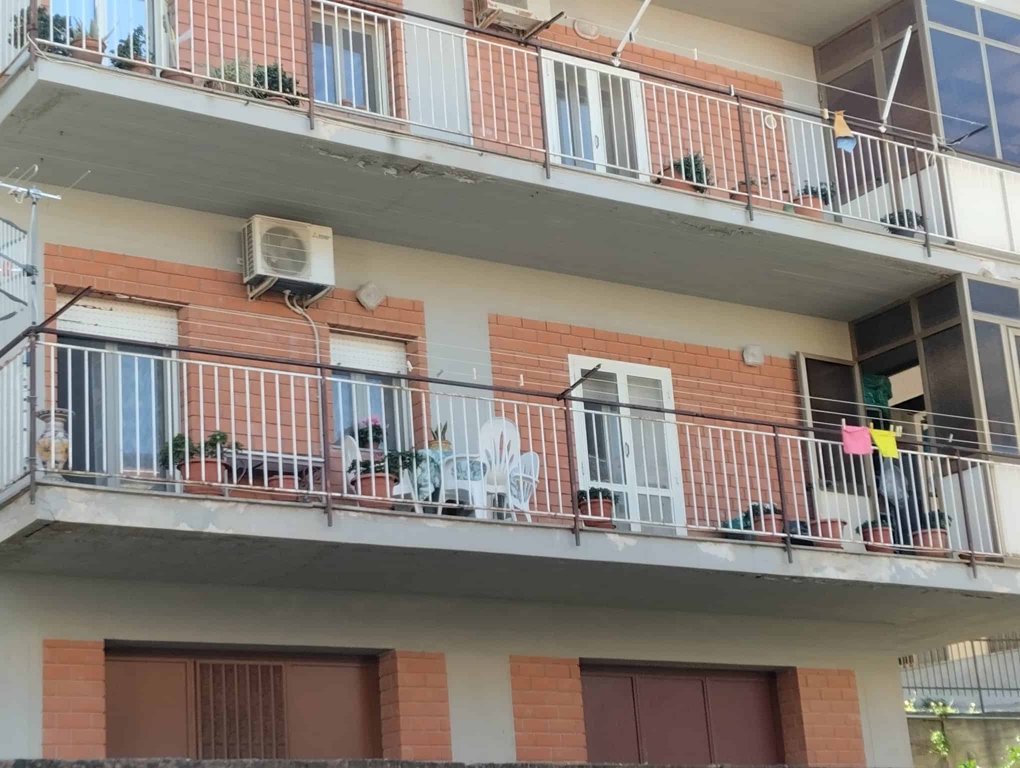 Appartamento con balcone in edificio residenziale, vista esterna, con arredi e piante, in un contesto urbano moderno.