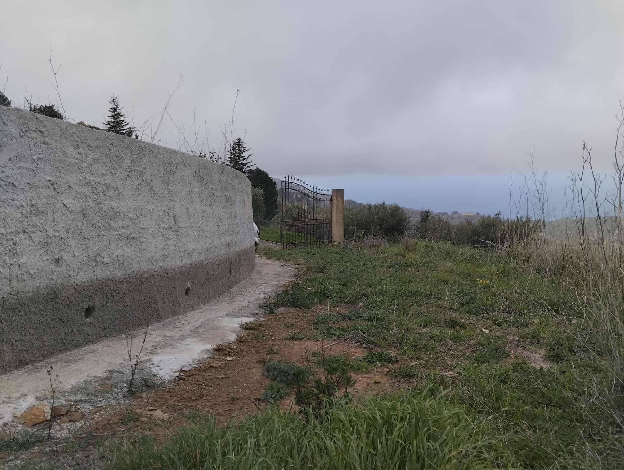 Barriera in cemento e cancello in ferro su un sentiero rurale con paesaggio naturale e cielo nuvoloso, ideale per immagini di proprietà rurali o terreni in vendita in Italia.