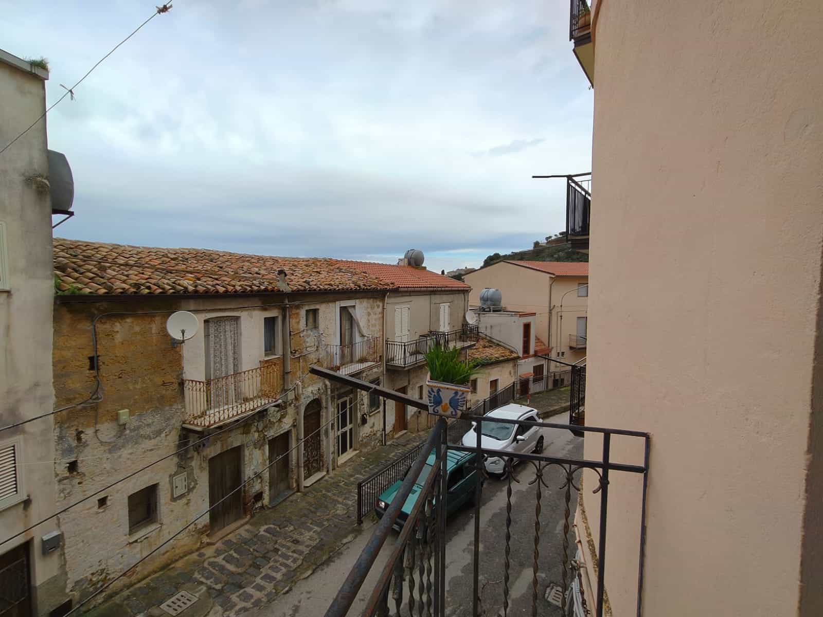 Balcone con vista su strada storica in un quartiere residenziale di città italiana, con edifici tradizionali e auto parcheggiate, sotto un cielo nuvoloso.