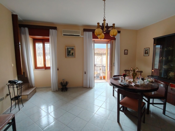 Interno soggiorno luminoso con grandi finestre e accesso al balcone, arredato con tavolo e sedie, decorazioni classiche e aria condizionata, ideale per vivere in comfort.