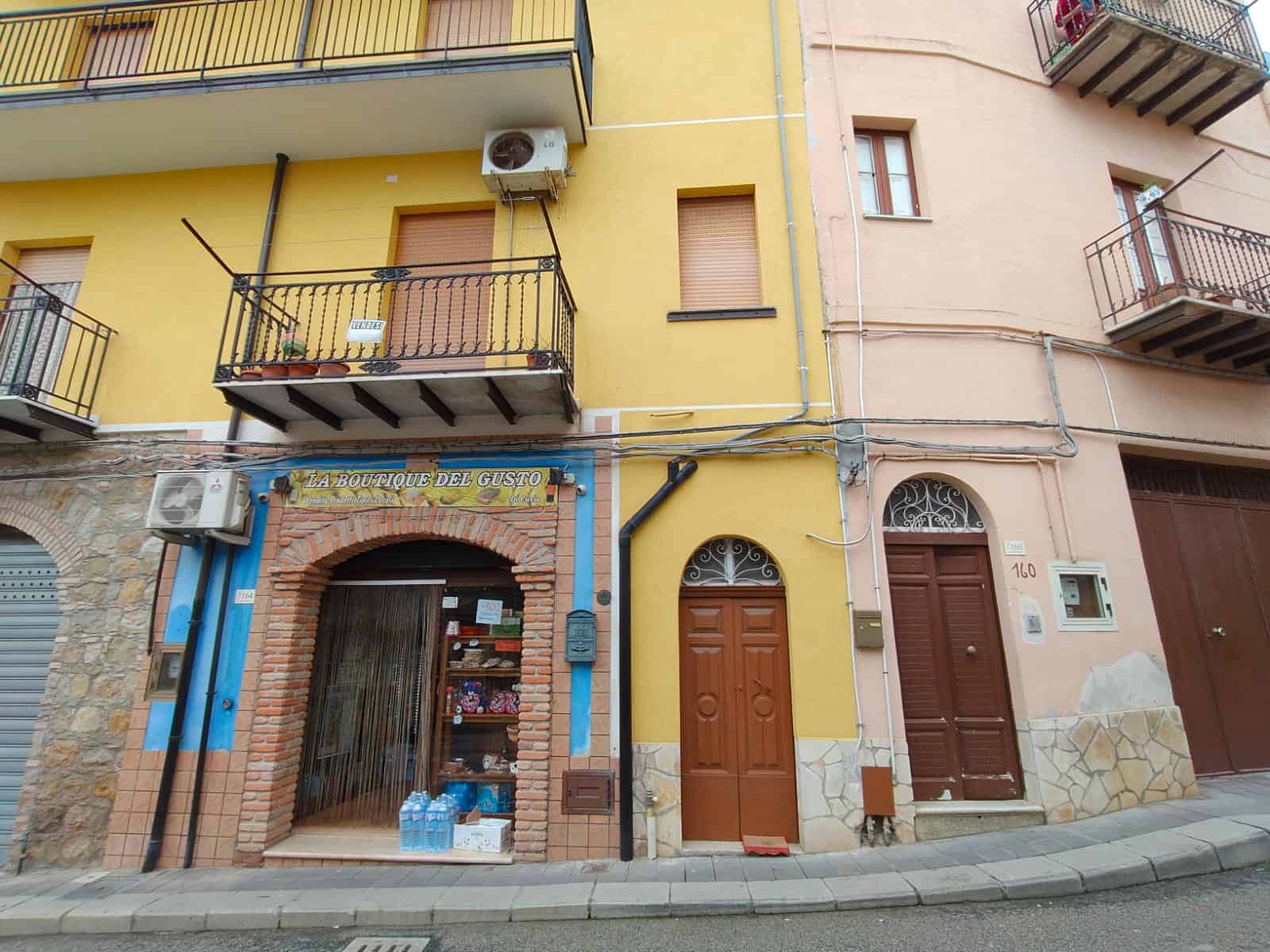Porte e facciata di un edificio residenziale con negozio al piano terra, balconi con ringhiere in ferro, pareti gialle e dettagli in pietra, in un contesto urbano italiano.