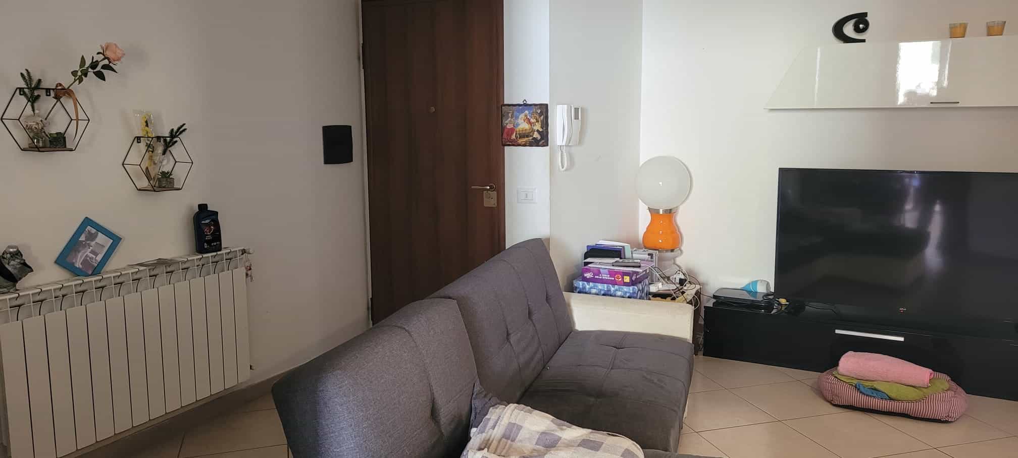 Spazio living moderno con divano grigio, televisore a schermo piatto e decorazioni eleganti, ideale per ambienti accoglienti e funzionali.