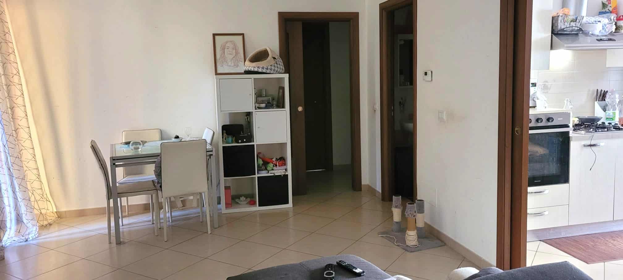 Ampia vista di un soggiorno con zona pranzo e cucina in stile moderno, illuminato da luce naturale, con mobili funzionali e decorazioni minimaliste.