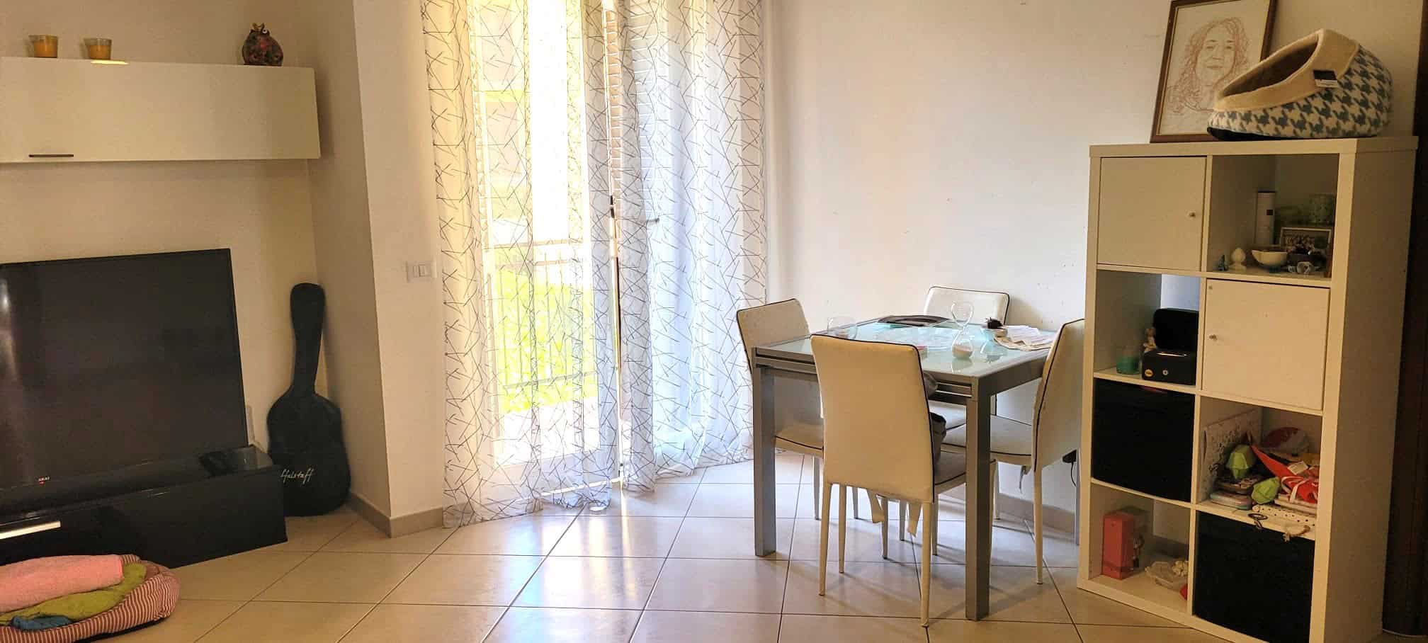 Ampia zona living con tavolo da pranzo, soggiorno luminoso e arredi moderni, ideale per famiglie e coppie, con accesso a balcone e spazio per relax e convivialità.