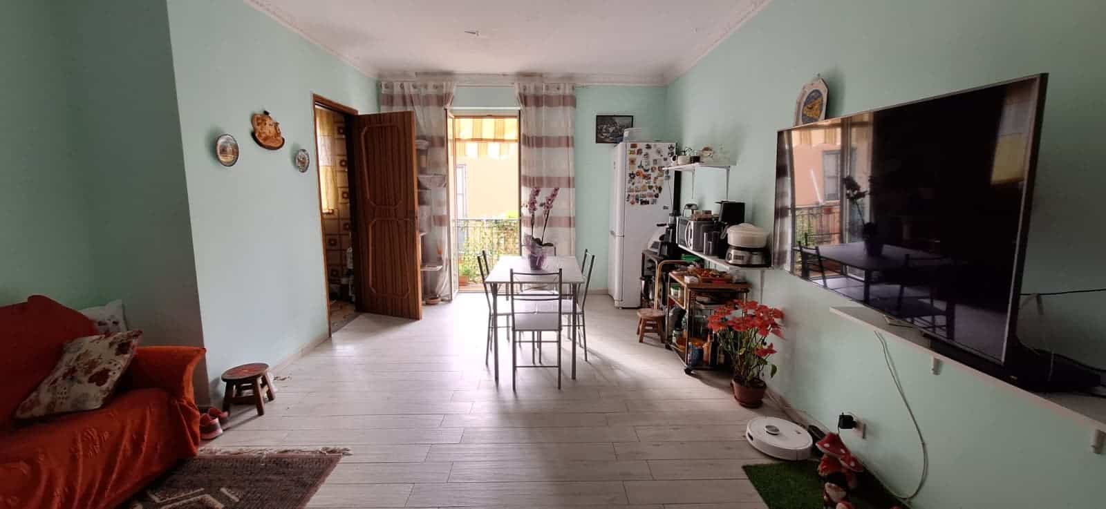 Ampia sala living luminosa con divano, tavolo e sedie, TV a schermo piatto e decorazioni floreali, ideale per relax e intrattenimento in un ambiente accogliente e ben arredato.