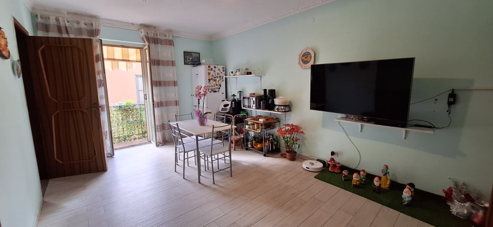 Ampio soggiorno luminoso con balcone, arredato con tavolo, sedie, TV a schermo piatto e decorazioni natalizie, ideale per vivere momenti di relax e convivialità in un ambiente accogliente.