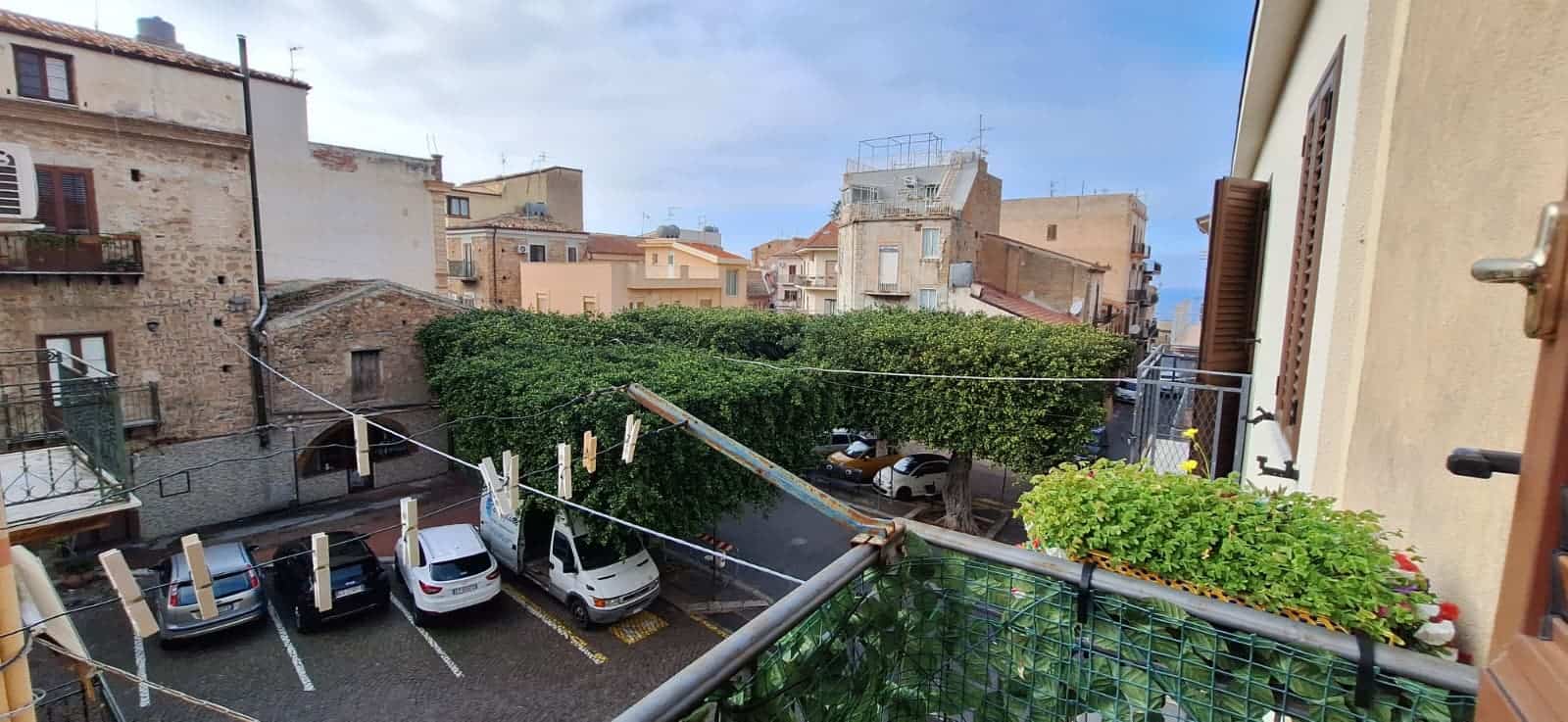 Vista di un cortile interno con parcheggio e piante verdi, in un quartiere residenziale di città, con edifici storici e moderni sullo sfondo, in una giornata soleggiata.
