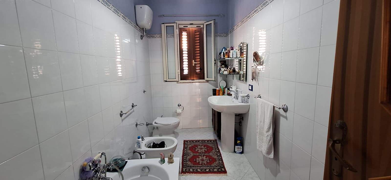 Lavabo e bidet in un bagno spazioso con pareti e pavimenti bianchi, specchio sopra il lavabo e accessori per il bagno.