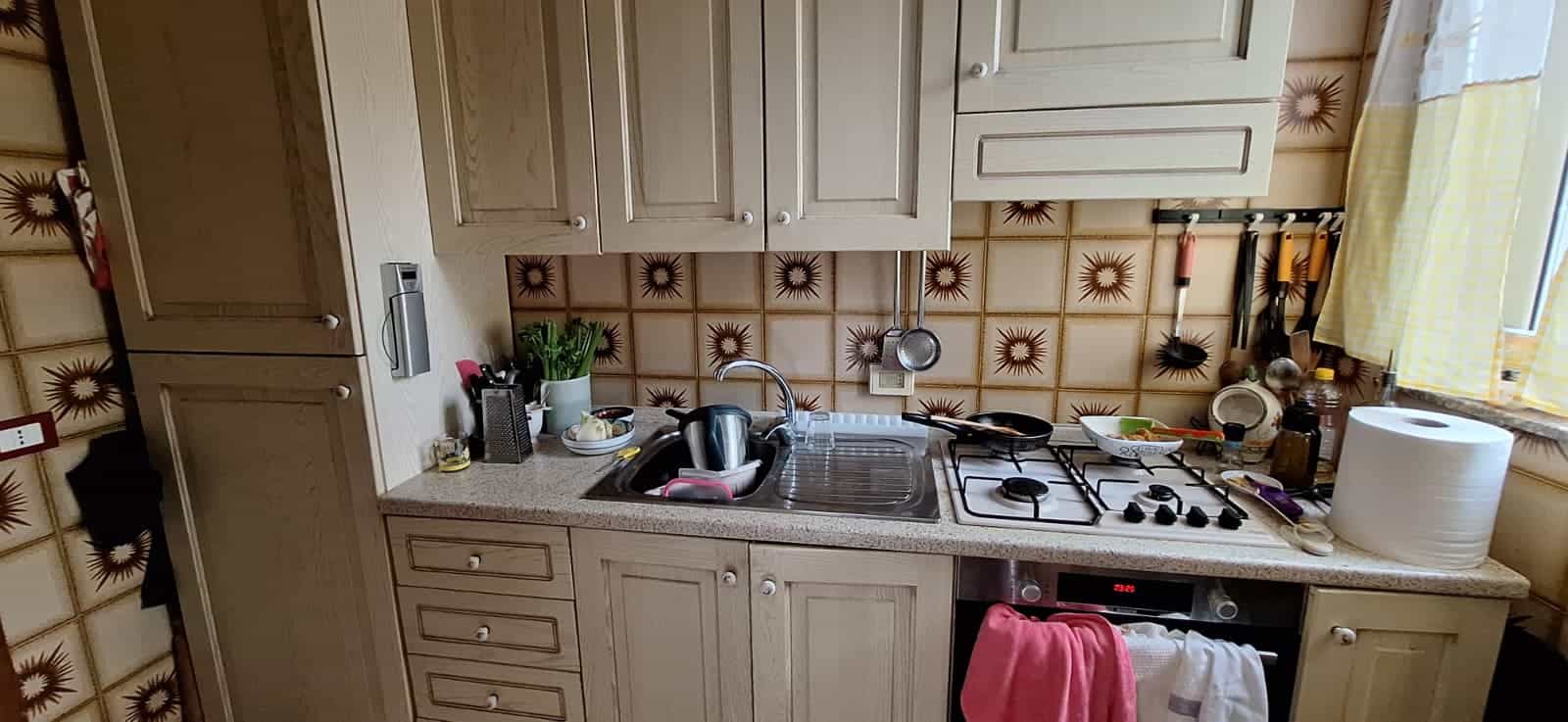 Lavello e piano cottura in cucina con utensili e stoviglie, ambiente domestico accogliente e funzionale.