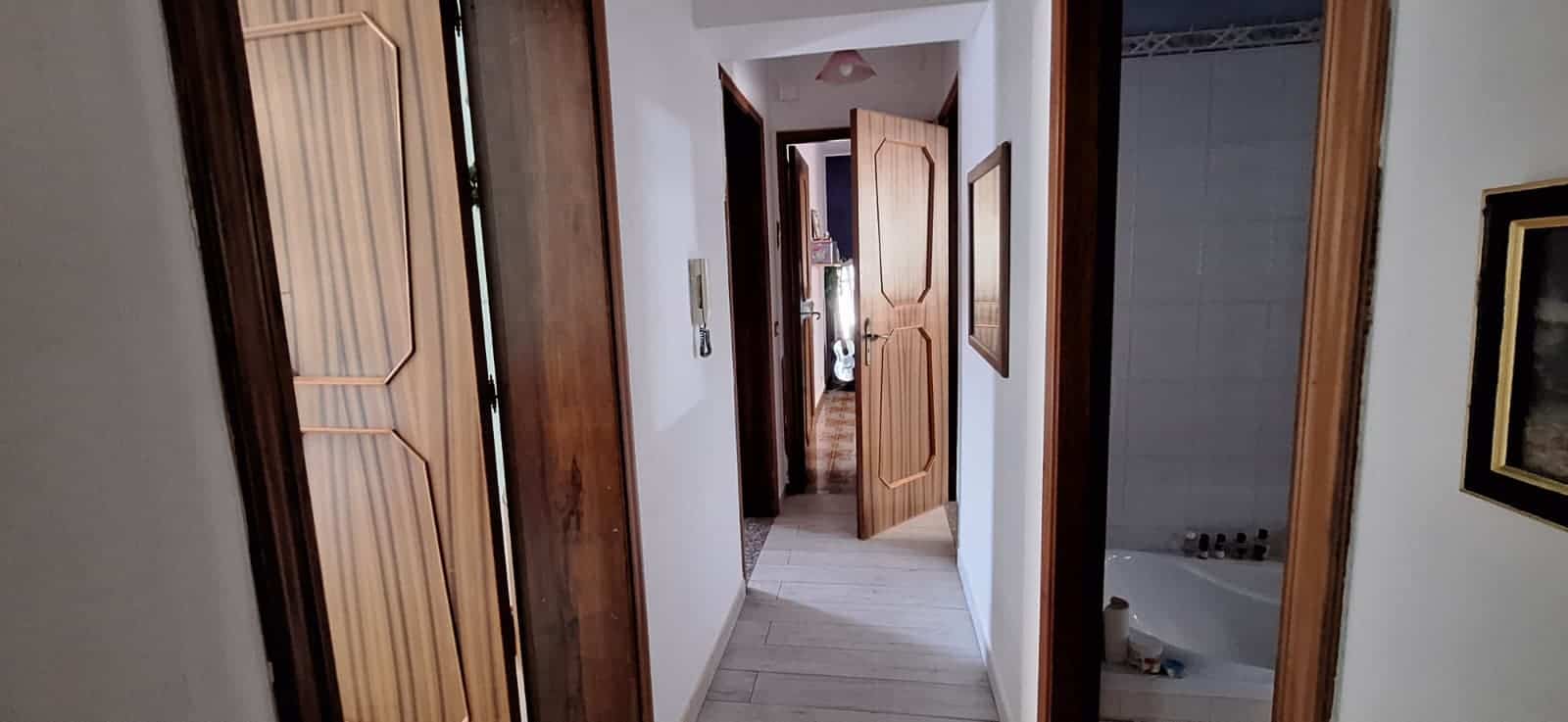 Ampia vista di un corridoio interno di una casa, con porte in legno e pareti bianche, che conduce a diverse stanze, con un ambiente luminoso e accogliente.