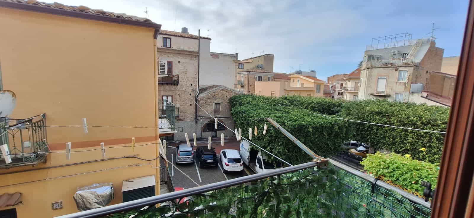 Balcone con vista su cortile e edifici storici, in un quartiere residenziale di città italiana, con linee di lavanderia stese e veicoli parcheggiati, sotto un cielo parzialmente nuvoloso.
