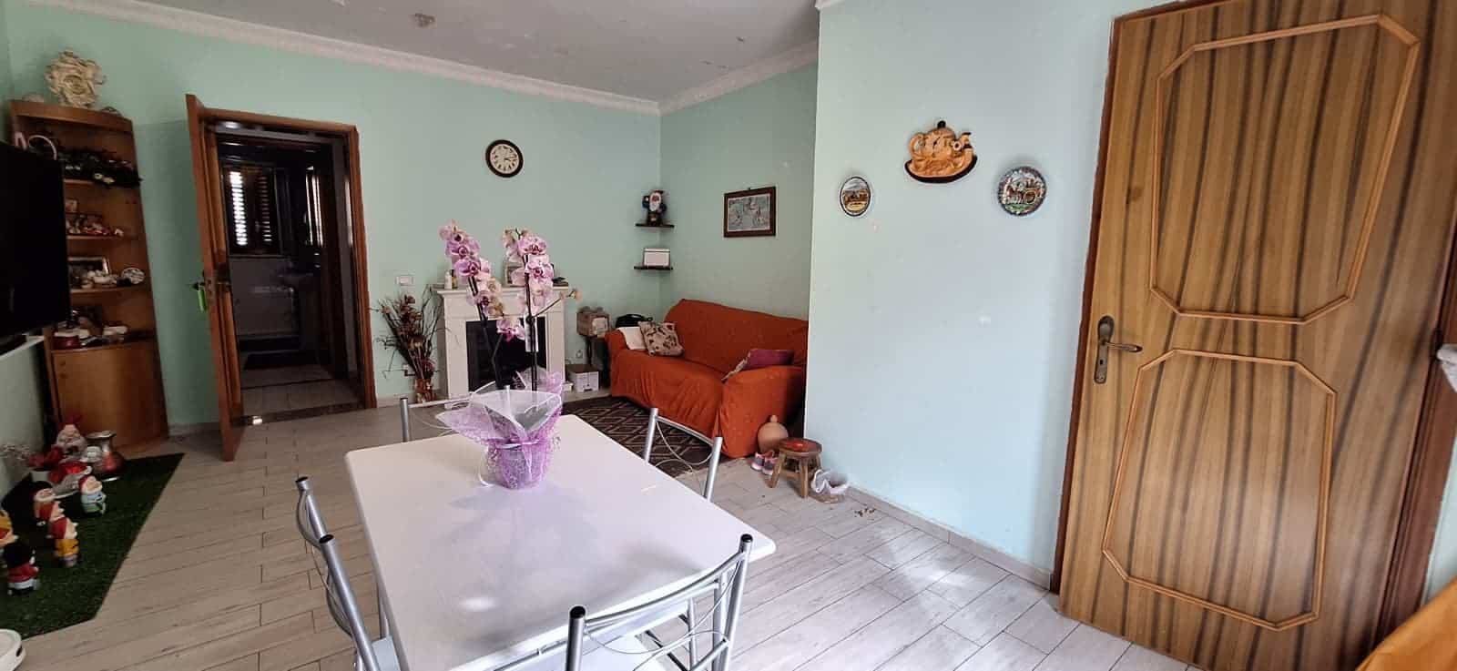 Ampia stanza soggiorno con tavolo da pranzo, divano arancione e decorazioni floreali, ambiente luminoso e accogliente, ideale per vivere momenti di relax e convivialità.