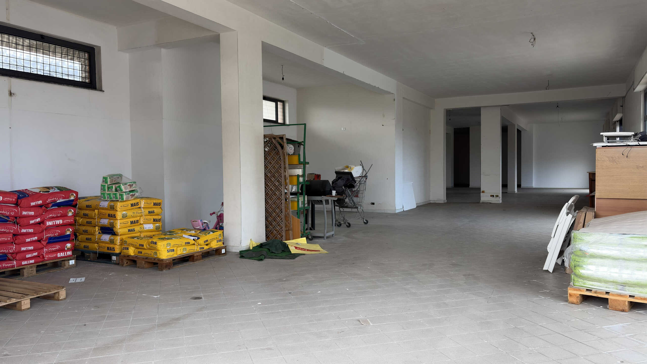 Ampio spazio commerciale o ufficio in fase di finitura, con pareti bianche e pavimento in piastrelle grigie, pronto per personalizzazione e allestimento. Ideale per attività commerciali o uffici moder.
