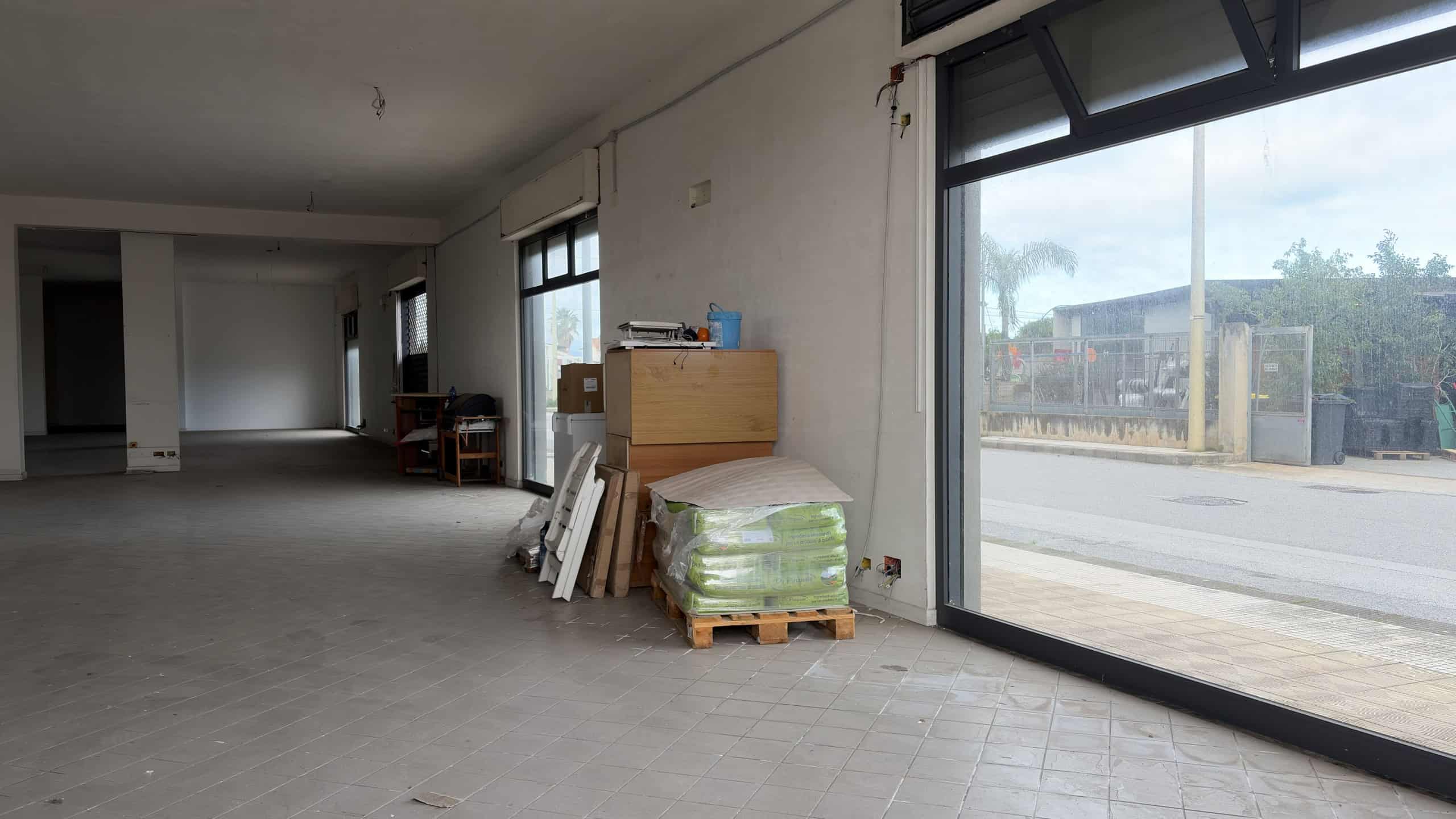 Ampio locale commerciale vuoto con grandi finestre e ingresso in vetro, pronto per allestimento o ristrutturazione, ideale per attività commerciali o uffici in zona strategica.