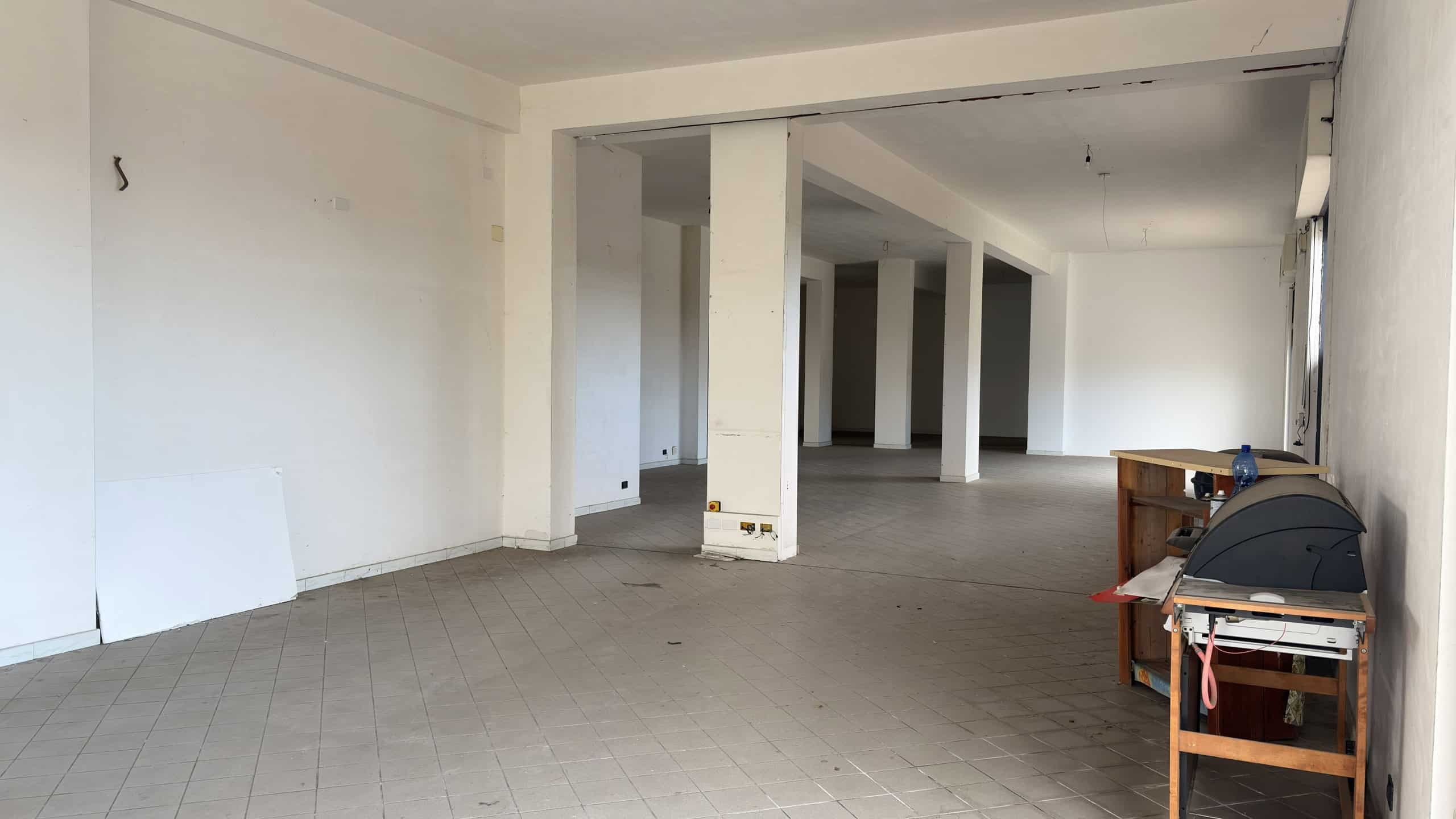 Ampia area commerciale o ufficio in open space con pareti bianche e pavimento in piastrelle, pronto per personalizzazione e arredamento. Ideale per attività commerciali o spazi di lavoro moderni.
