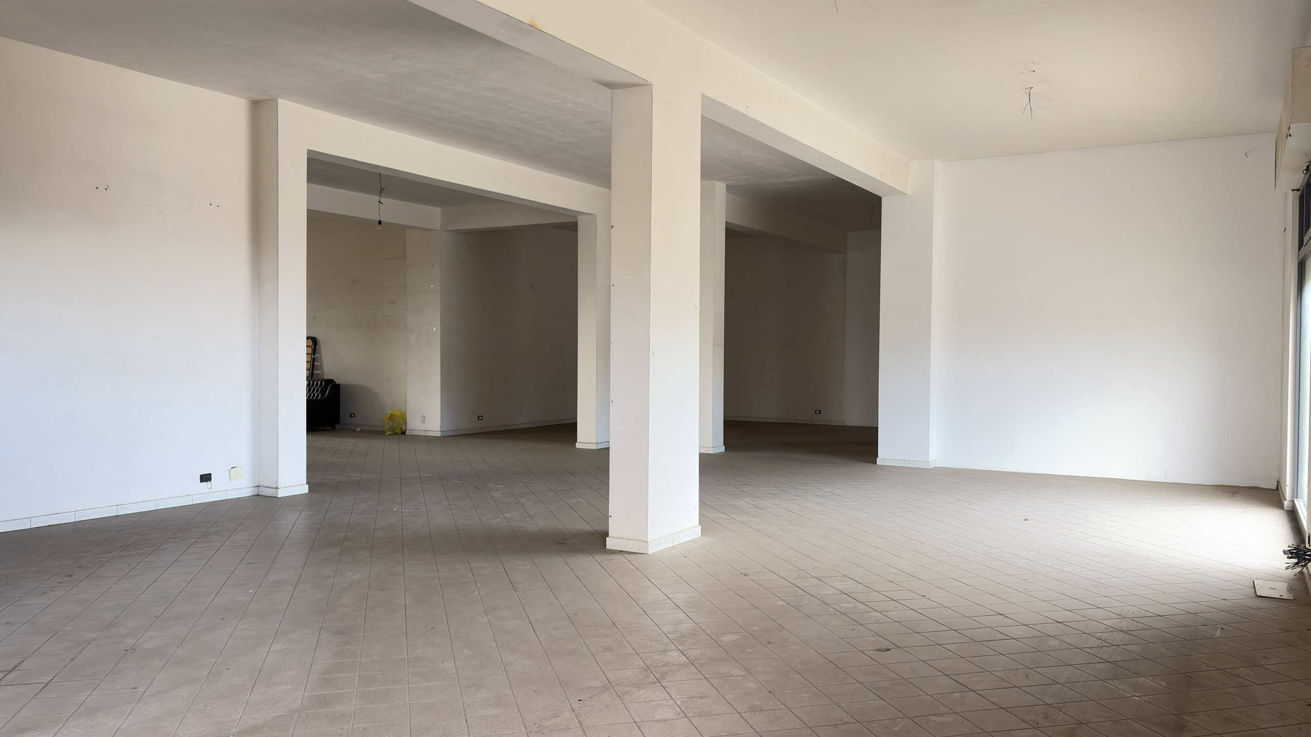 Ampia stanza vuota in un appartamento in costruzione, con pareti bianche e pavimento in piastrelle beige, pronta per essere personalizzata e arredato.