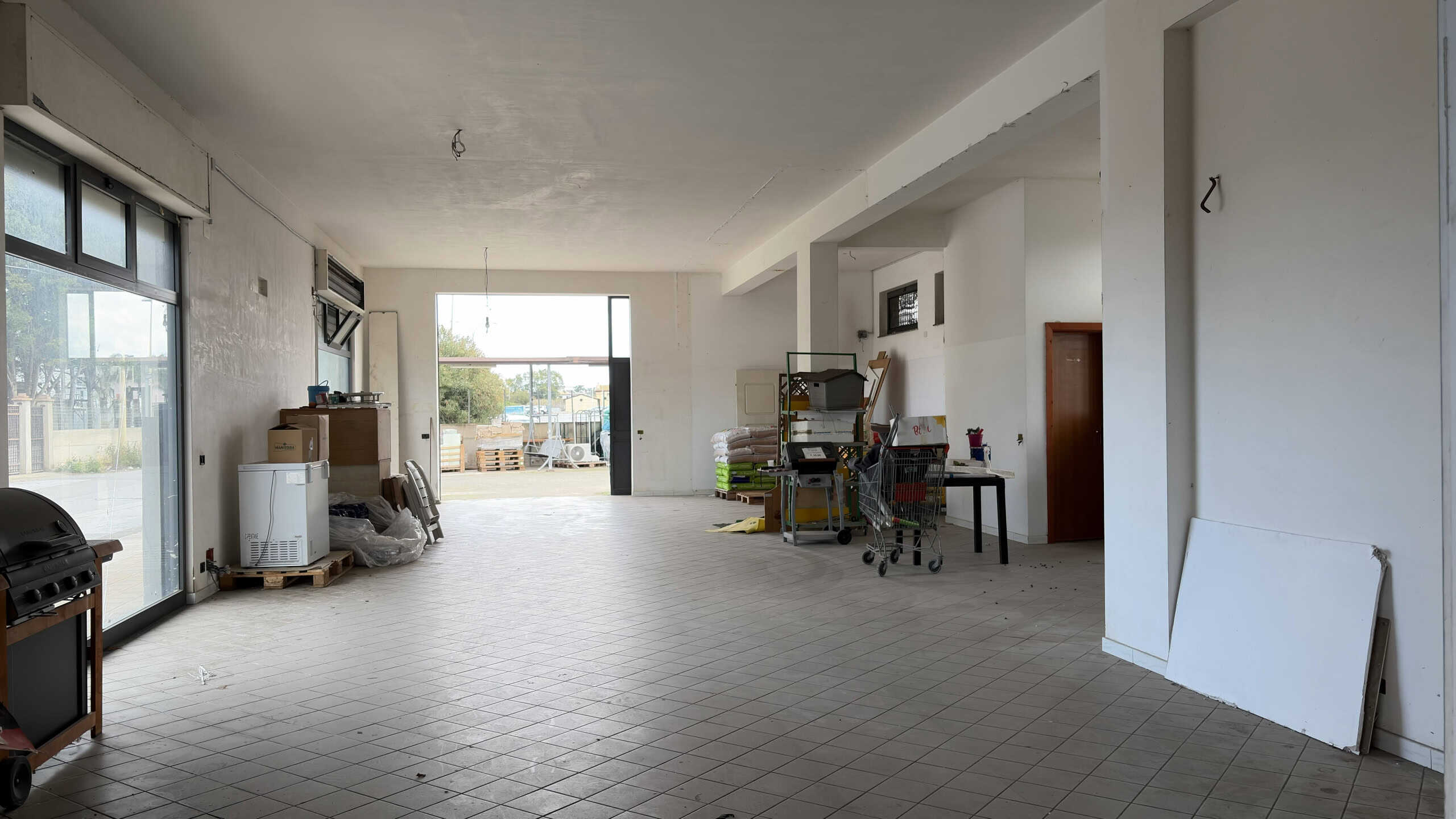 Ampio spazio interno di un appartamento in fase di ristrutturazione con pareti bianche, grandi finestre e pavimento in piastrelle, pronto per essere personalizzato e arredato.
