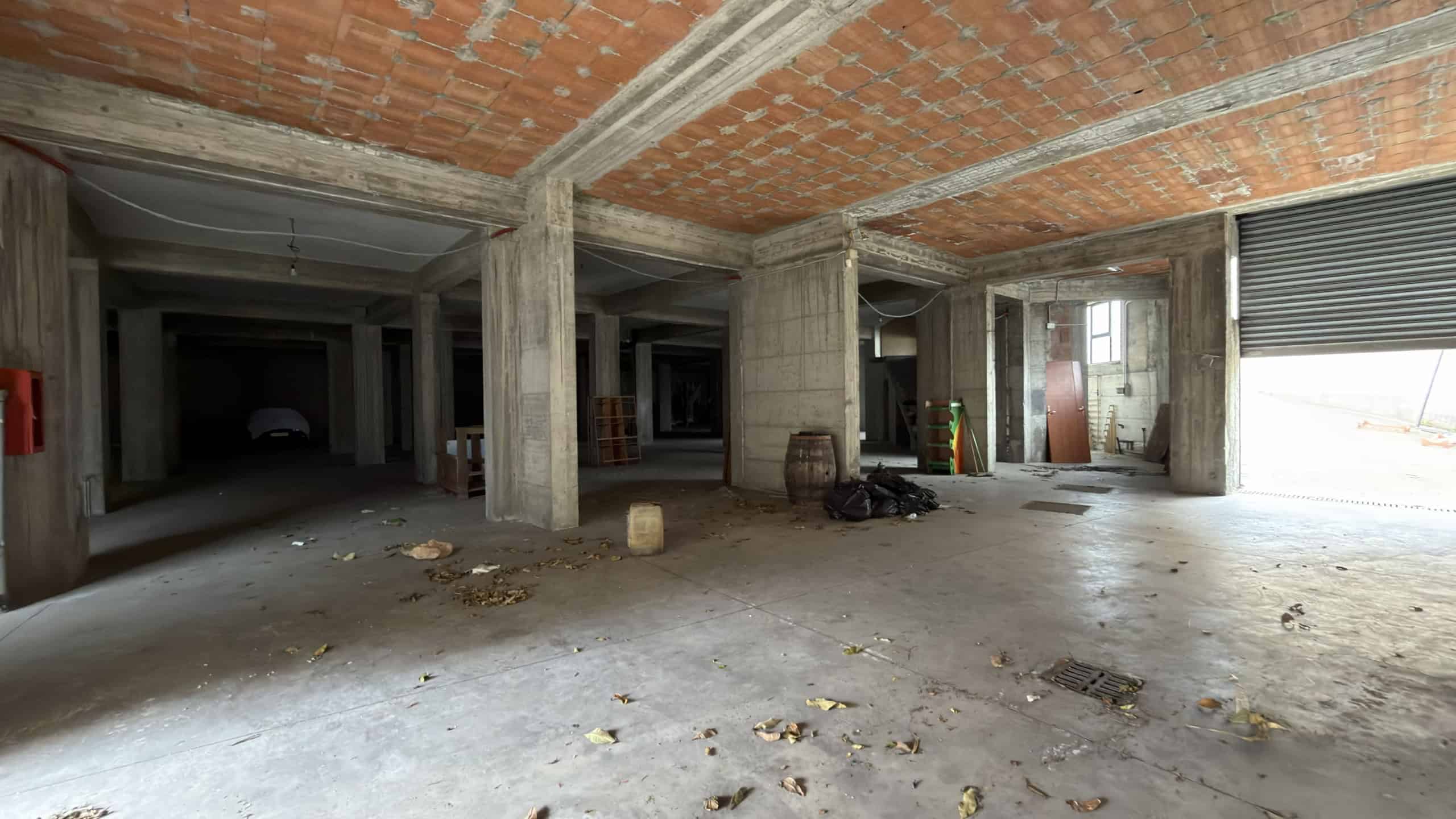 Ampio spazio commerciale in fase di ristrutturazione, con pareti in cemento e soffitto a vista, pronto per personalizzazioni e allestimenti. Ideale per attività commerciali o uffici moderni.