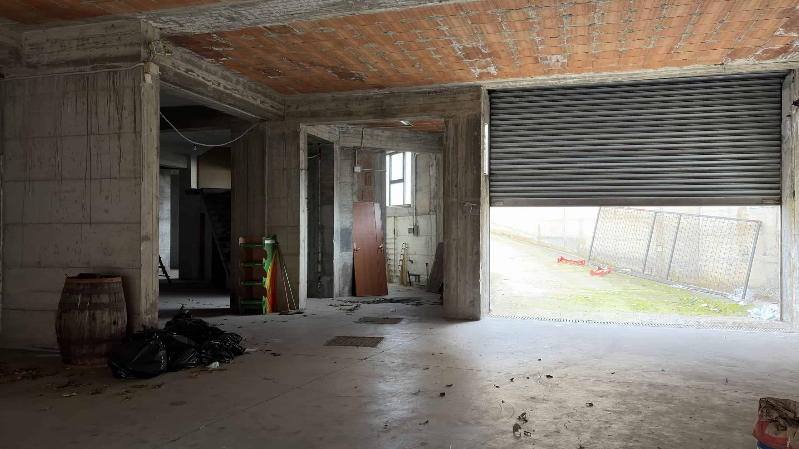 Immagine di un'area di cantiere in costruzione con pareti in cemento e un grande portone garage con serranda metallica parzialmente aperta.