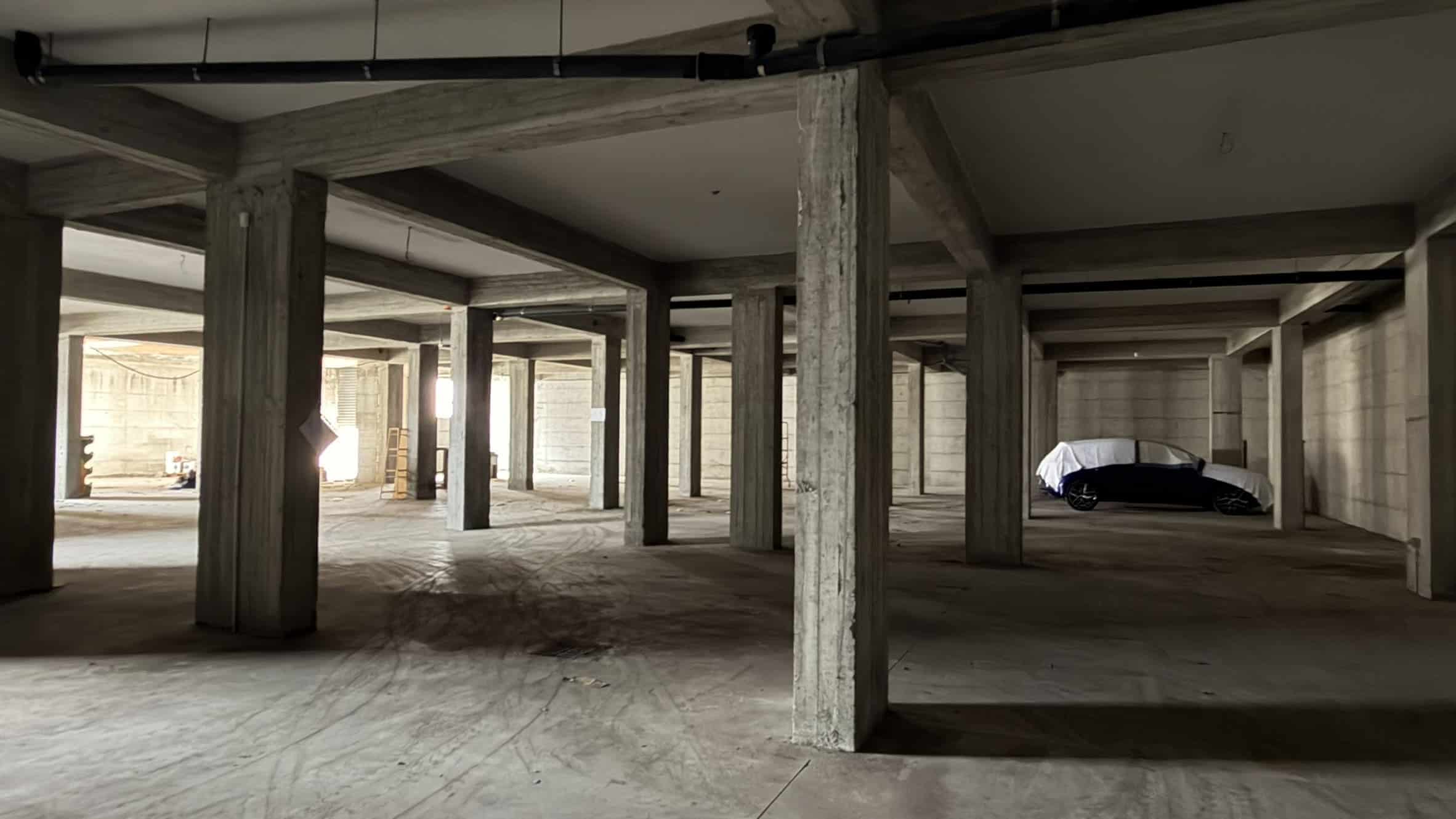 Porte aperte di un garage o parcheggio sotterraneo in costruzione con strutture in cemento e veicolo coperto in background.