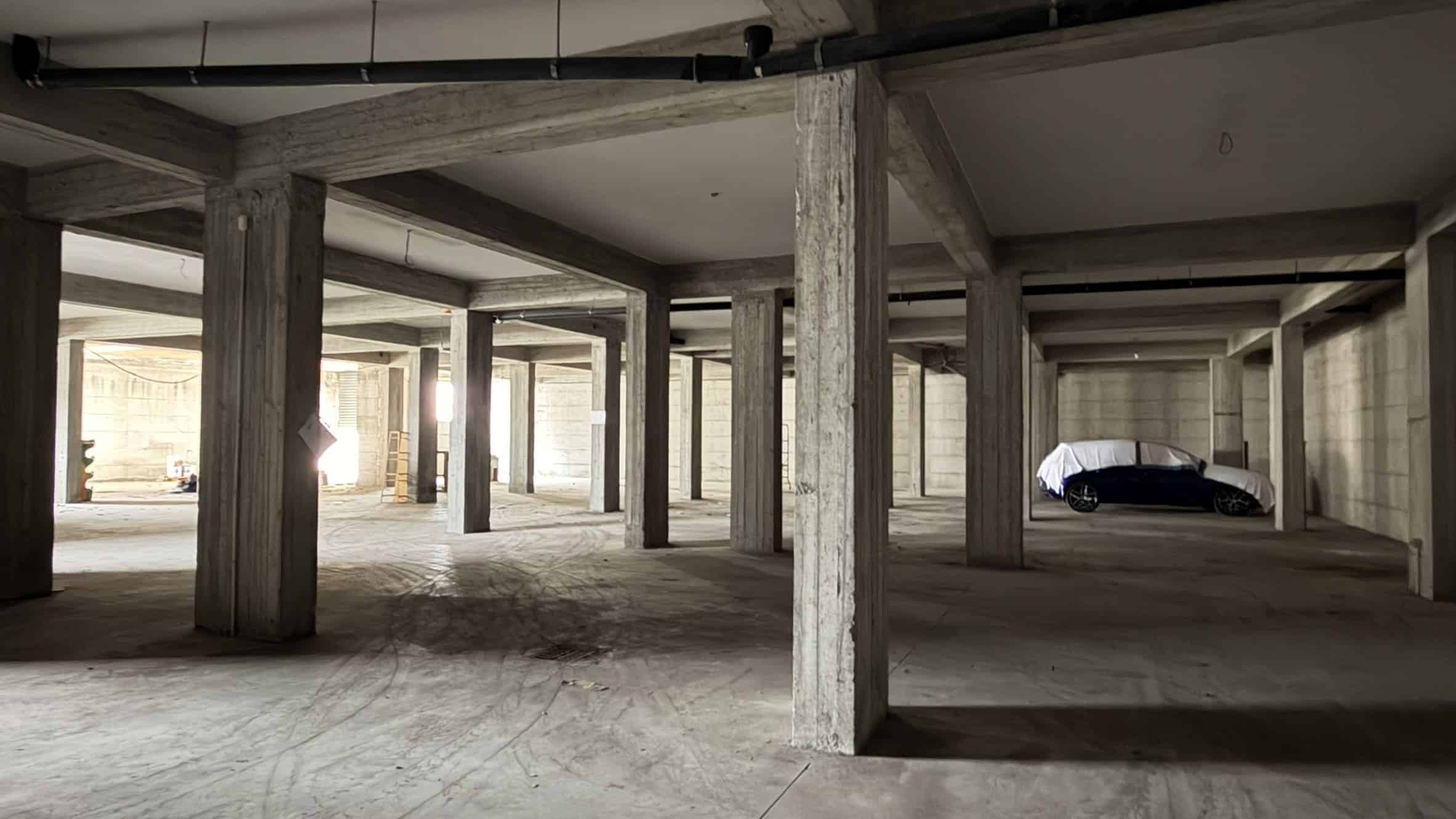 Pilastri in cemento e spazio vuoto in un parcheggio sotterraneo in costruzione, con luce naturale che entra dagli ingressi.