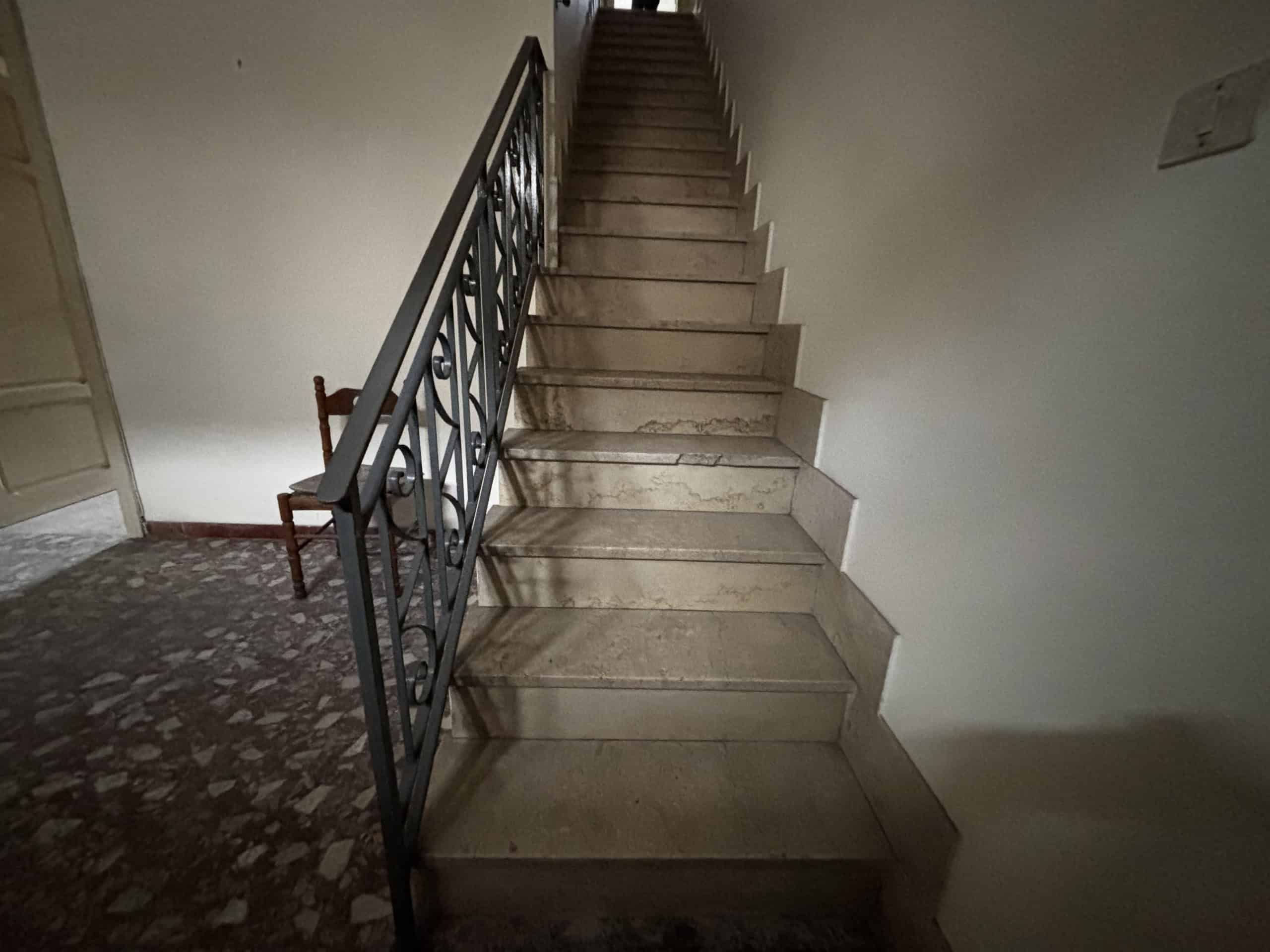 Escalier in pietra con ringhiera in metallo, interno di un edificio residenziale, vista dall'alto verso il basso.
