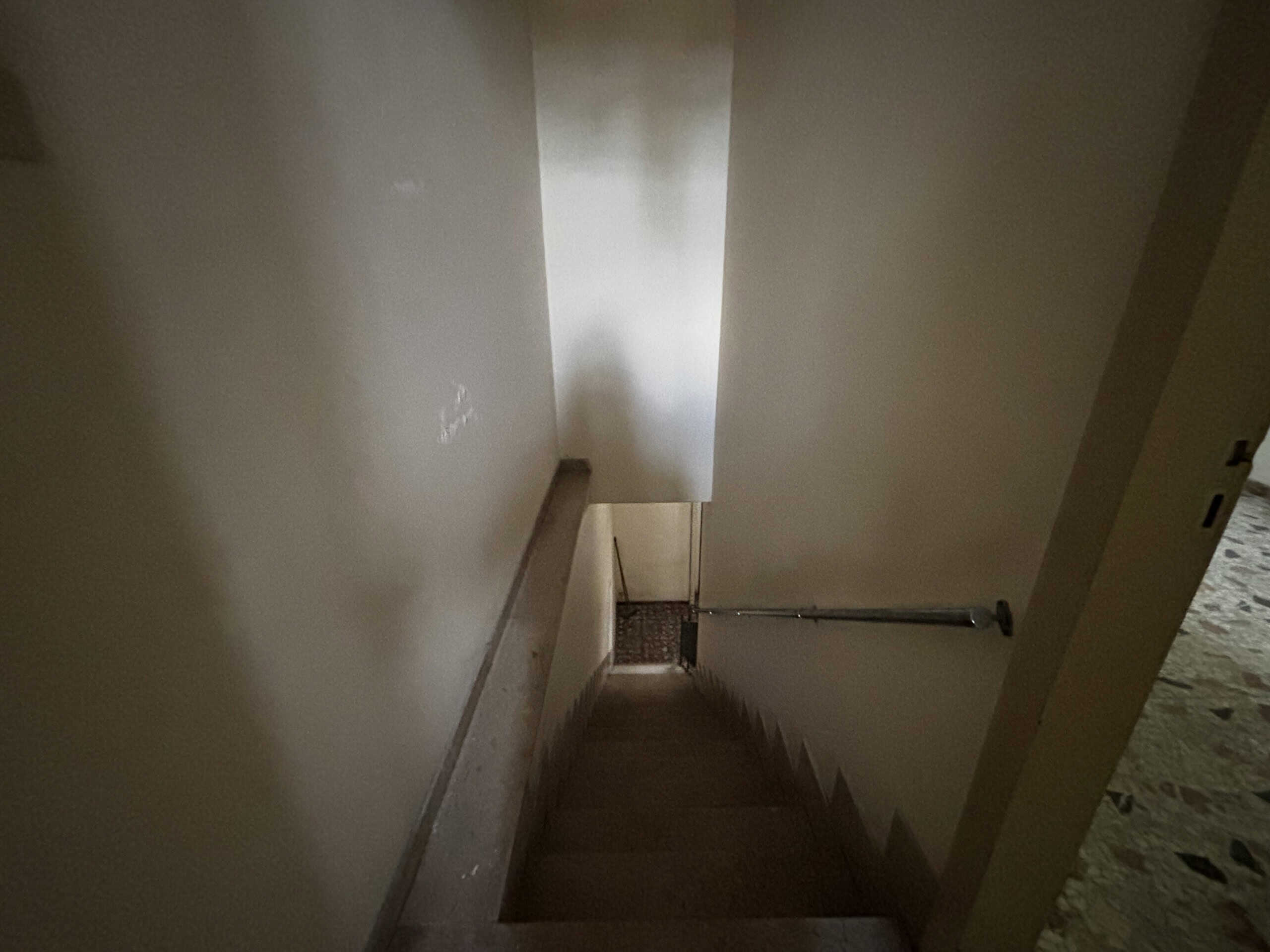 Scale interna di una casa con pareti beige e ringhiera in legno, vista verso il basso, illuminata da luce naturale.